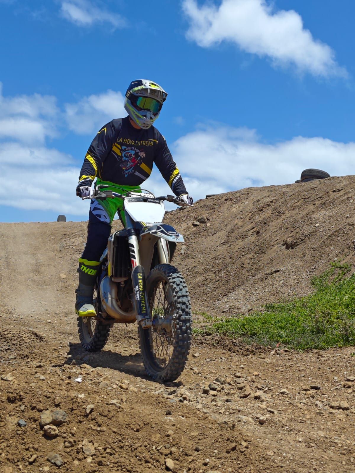 Piloto de motocross en una moto de tierra en un sendero rocoso bajo un cielo azul