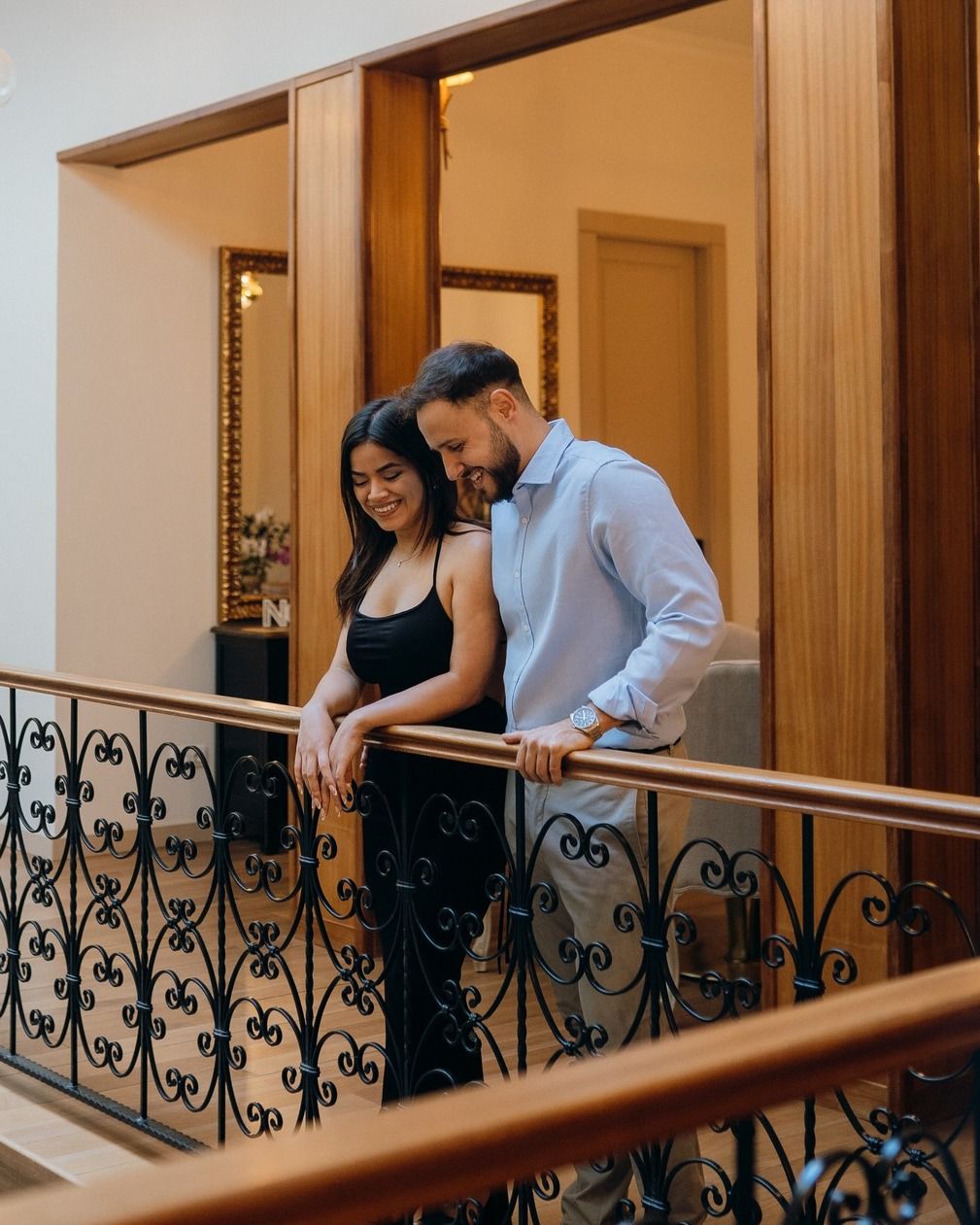 Pareja sonriendo en un balcón ornamentado de un pasillo cálidamente iluminado del hotel.