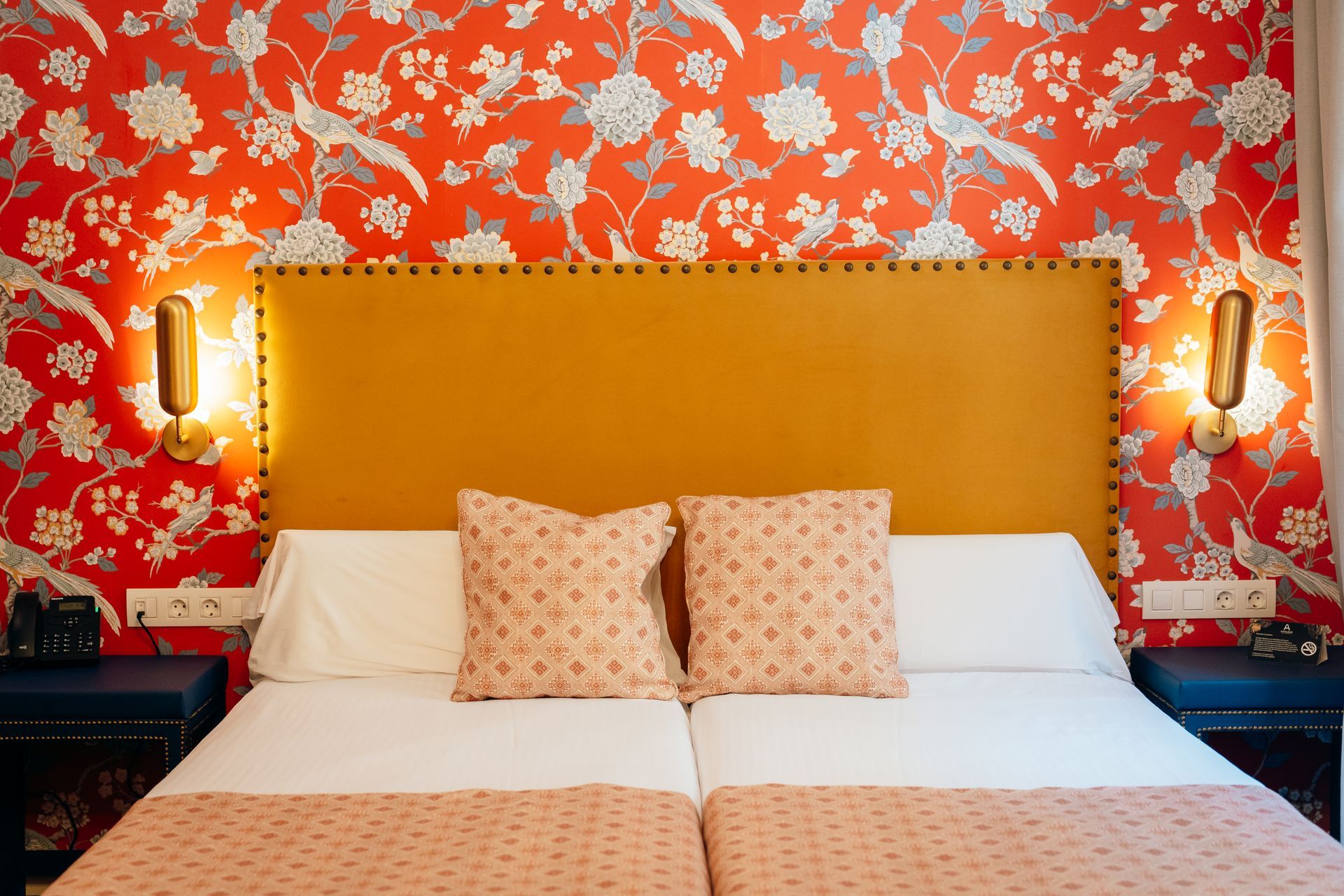 Habitación con papel pintado floral rojo, cabecero mostaza y cama impecablemente hecha con almohadas estampadas.
