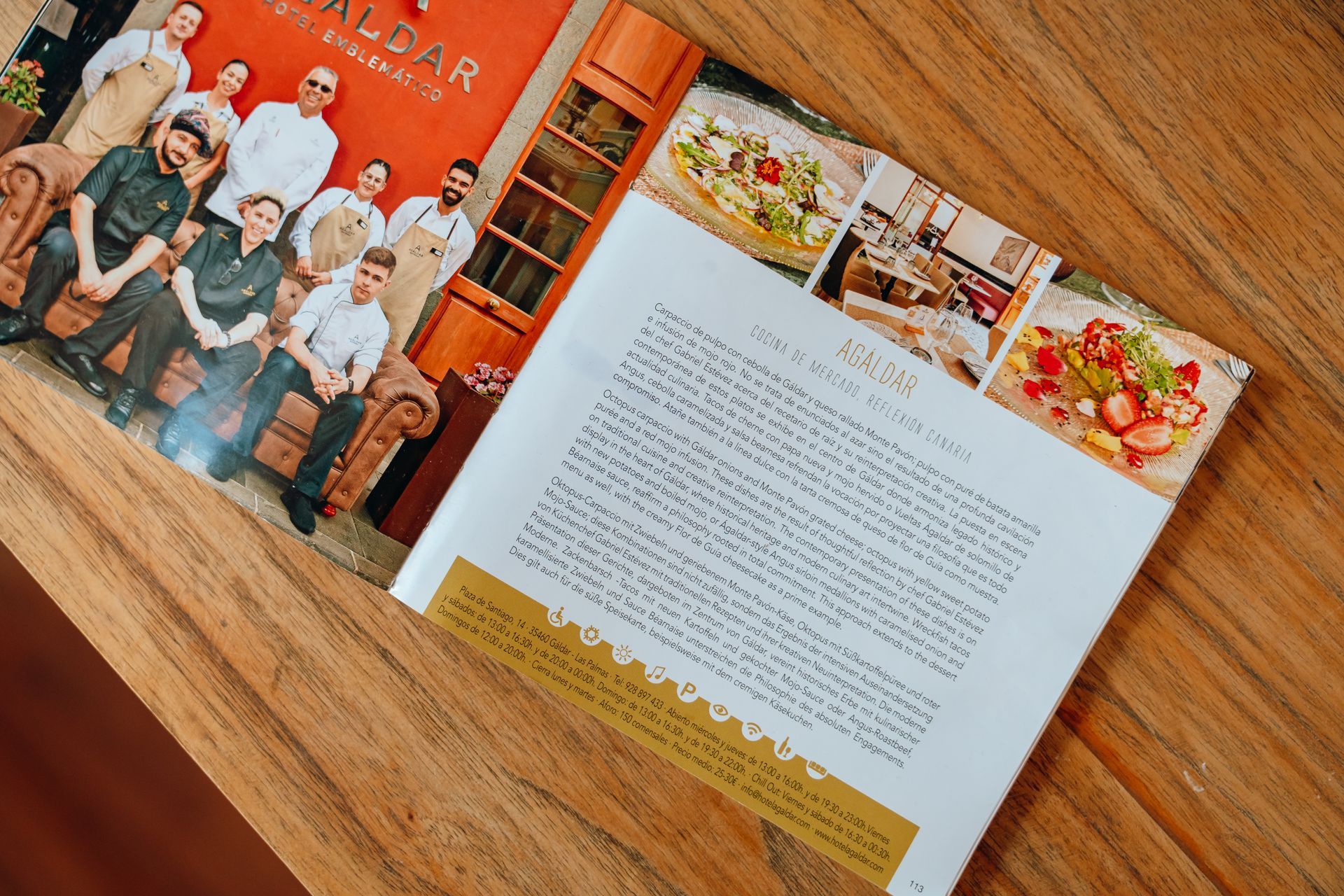 Libro de cocina abierto con una foto de grupo y una receta extendida sobre una mesa de madera.