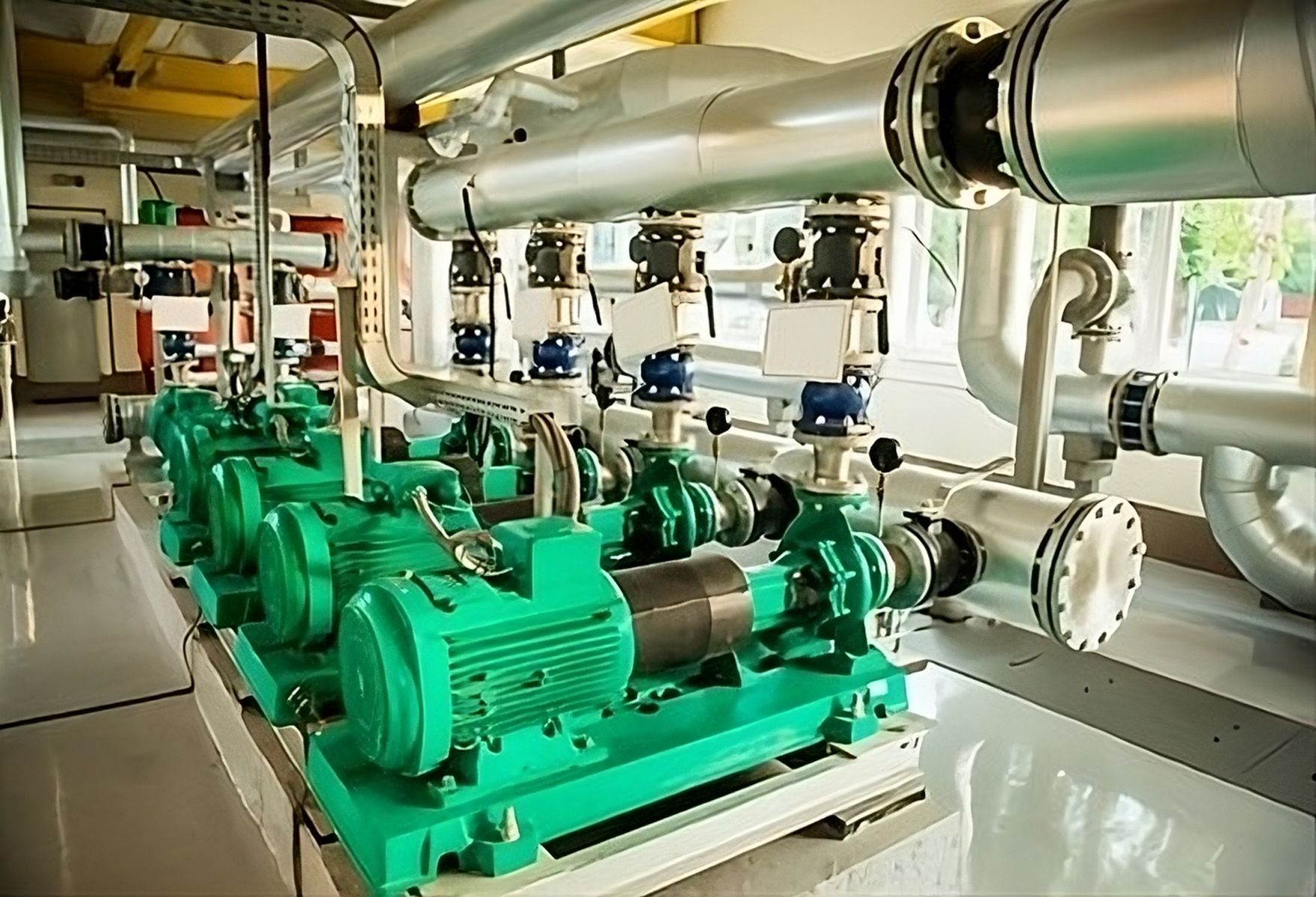 A row of green pumps are sitting in a room with pipes.