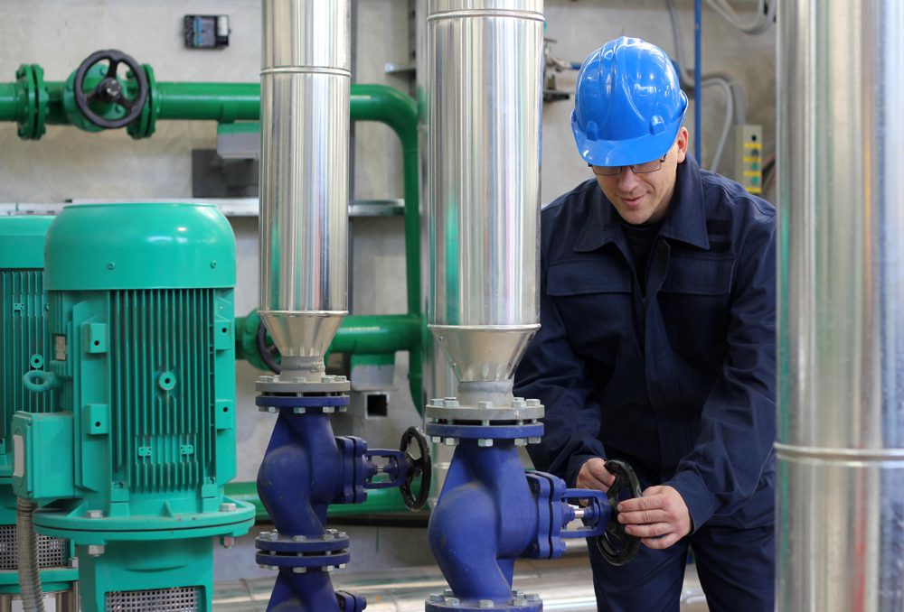 A man in a blue hard hat is working on a pump in a factory.