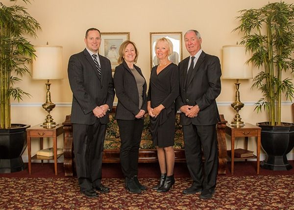 Four professionally dressed people posing indoors beside lamps and potted plants
