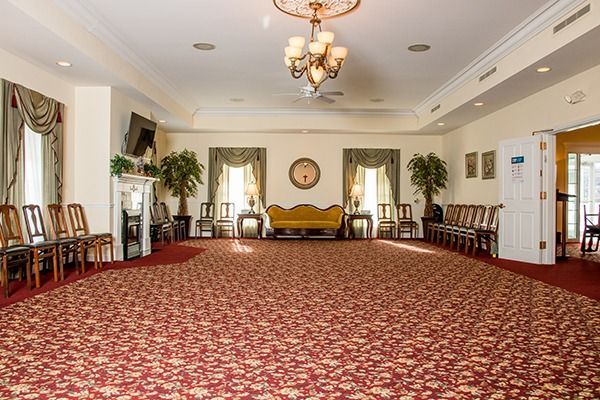 Large formal reception room with red carpet, gold sofas, chandeliers, and chairs along the walls