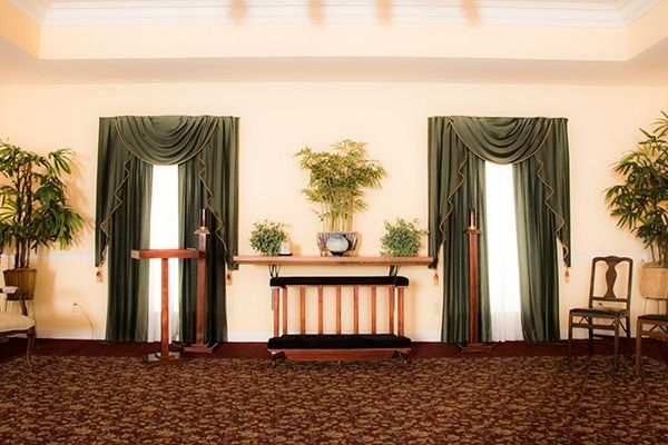 Empty stage with podium, green drapes, potted plants, and chairs in a formal room