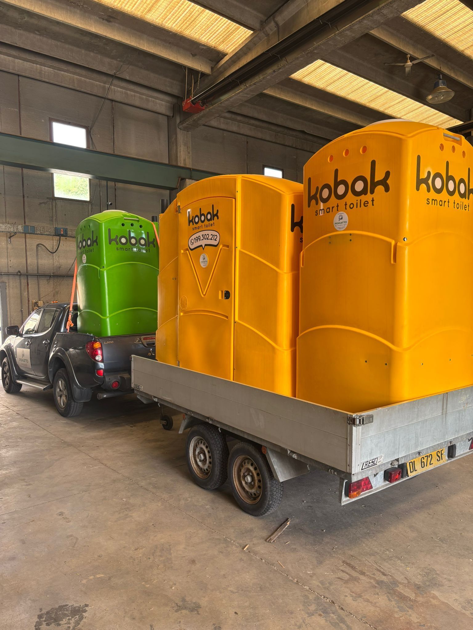 Camion che traina un rimorchio con tre bagni chimici: verde, giallo e giallo. Ambiente interno.