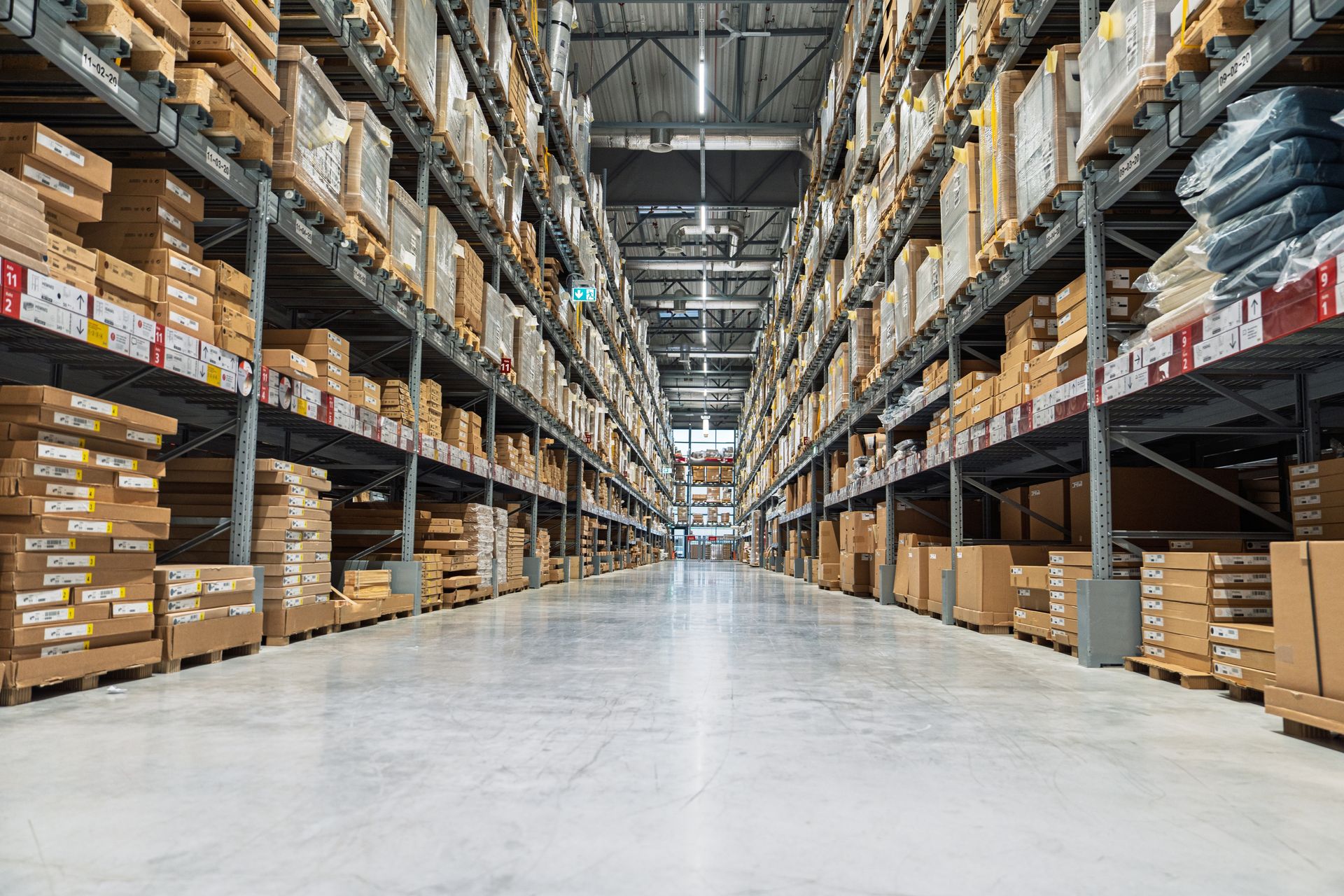 Aisle in a large warehouse with tall shelves of boxed goods stacked on both sides.