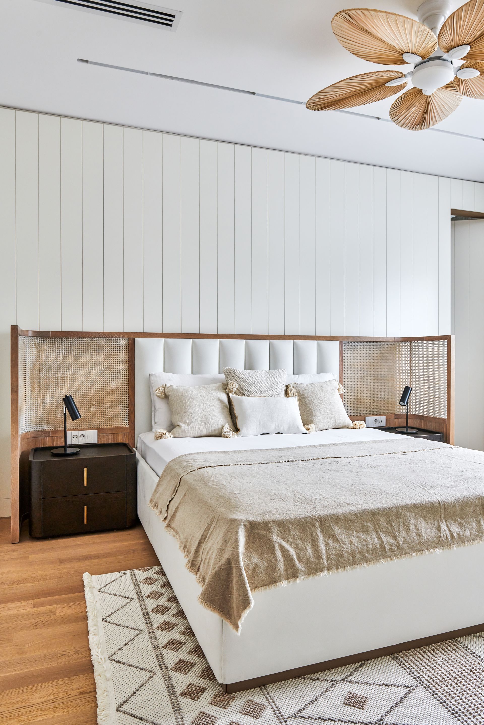 Modern bedroom with white upholstered bed, wood accent wall, and ceiling fan