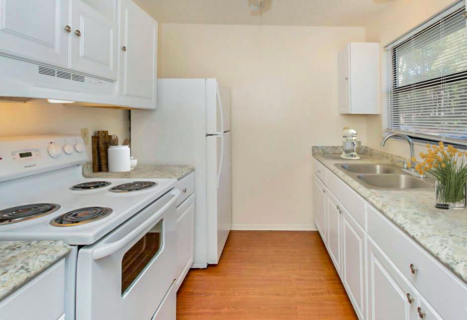 White kitchen with appliances, countertops, cabinets, and a window.