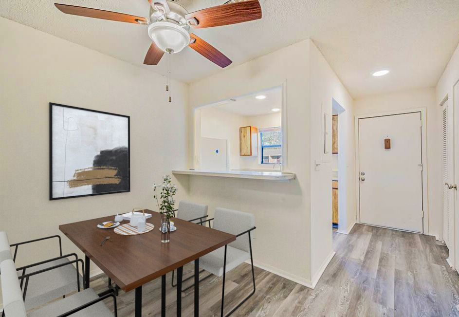 Dining area with table, chairs, art, and a pass-through to the kitchen. Hardwood floor and ceiling fan.