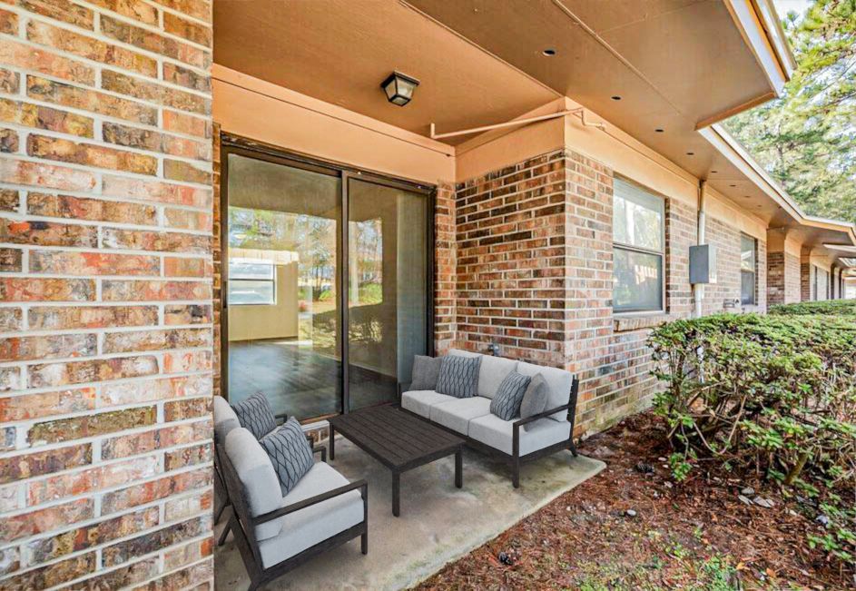 Outdoor patio with a seating set and sliding glass door. Brick building.