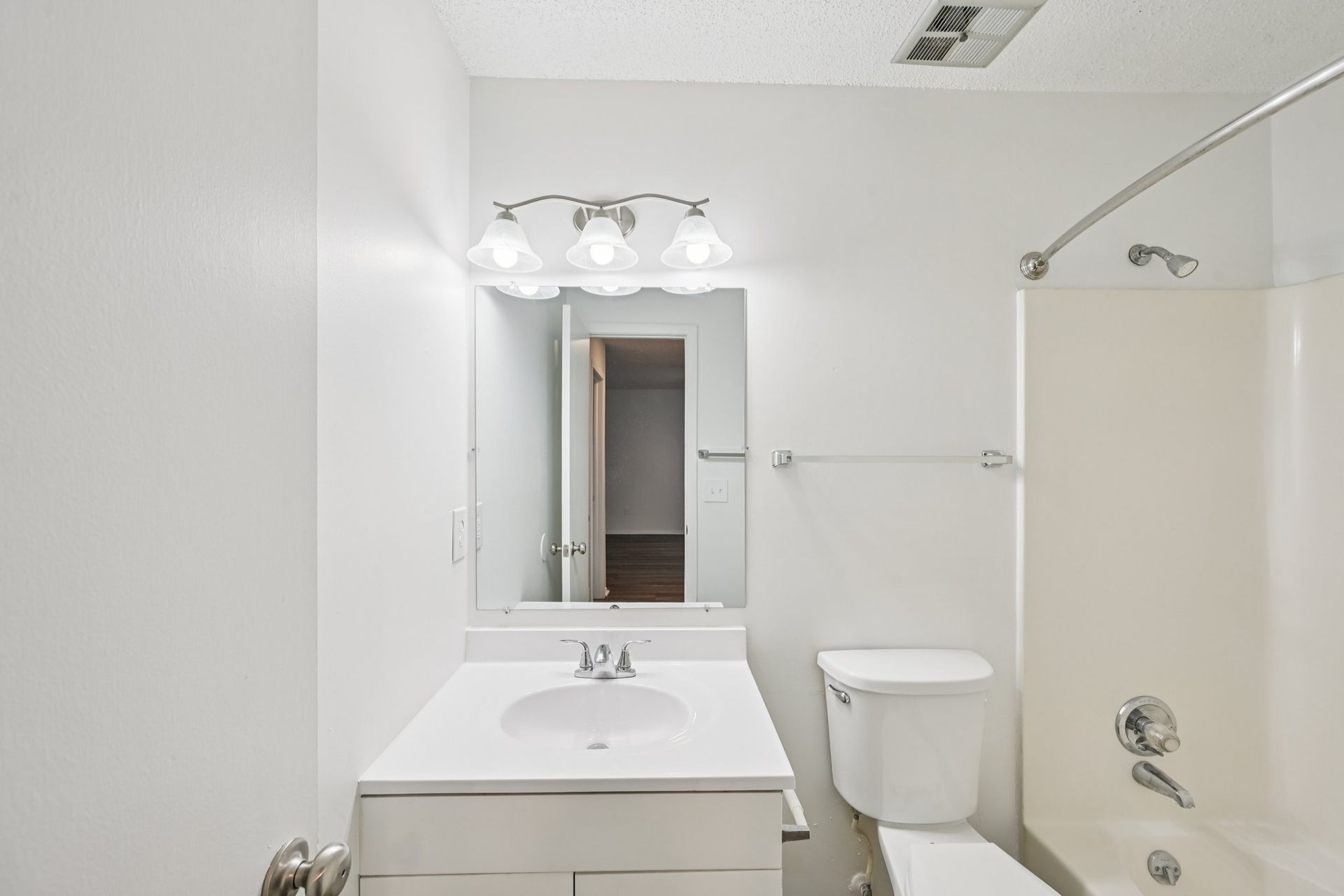 White bathroom with sink, toilet, tub, and mirror. Three-bulb light fixture above mirror.