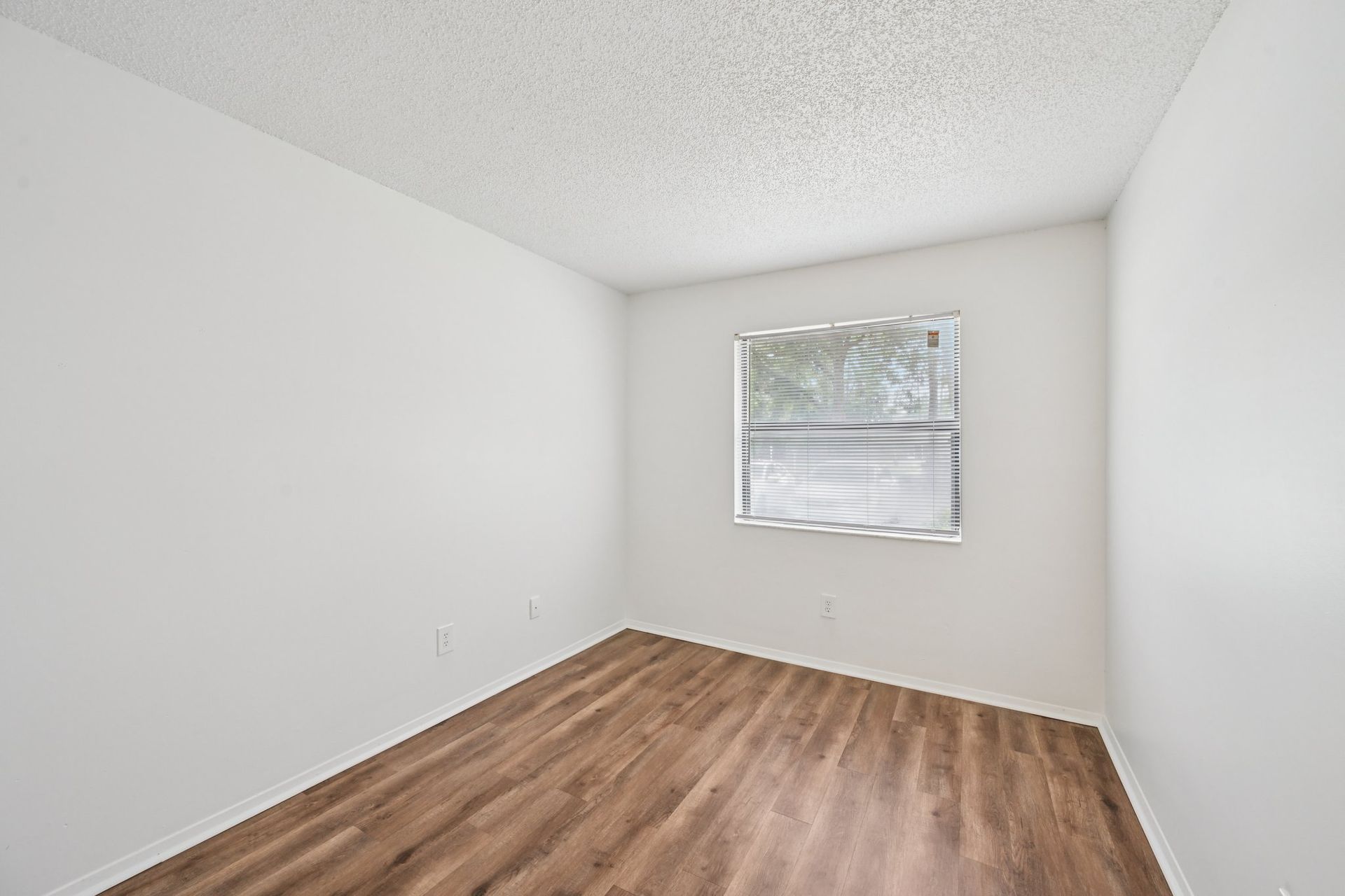 Empty room with wood-look floor, white walls, and a window with blinds.