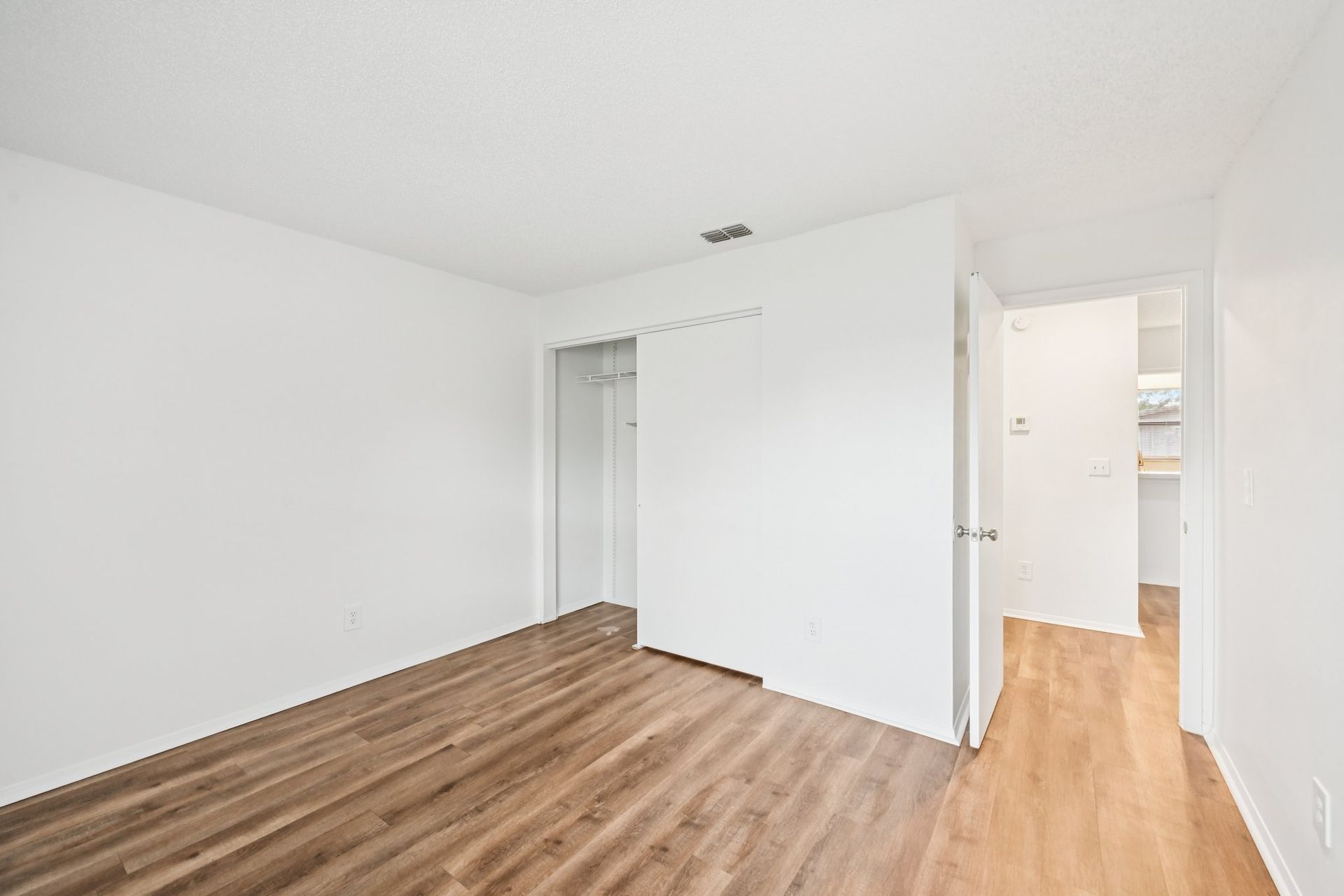 Empty room with wood-look flooring, white walls, closet, and doorway to another room.