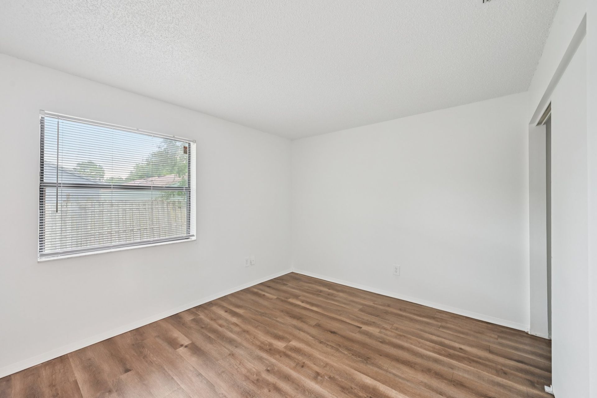Empty room with wood-look flooring, a window with blinds, and white walls.