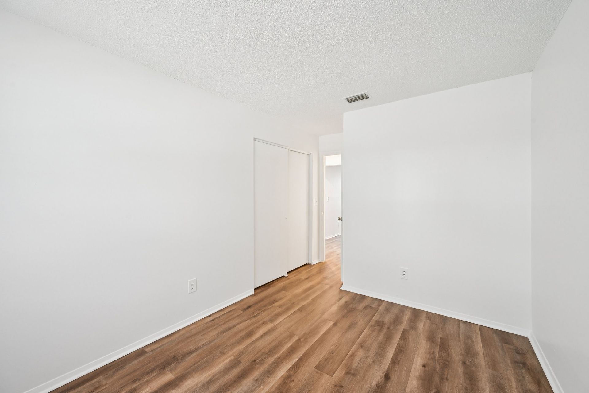 Empty room with white walls, wood-look flooring, and a doorway.