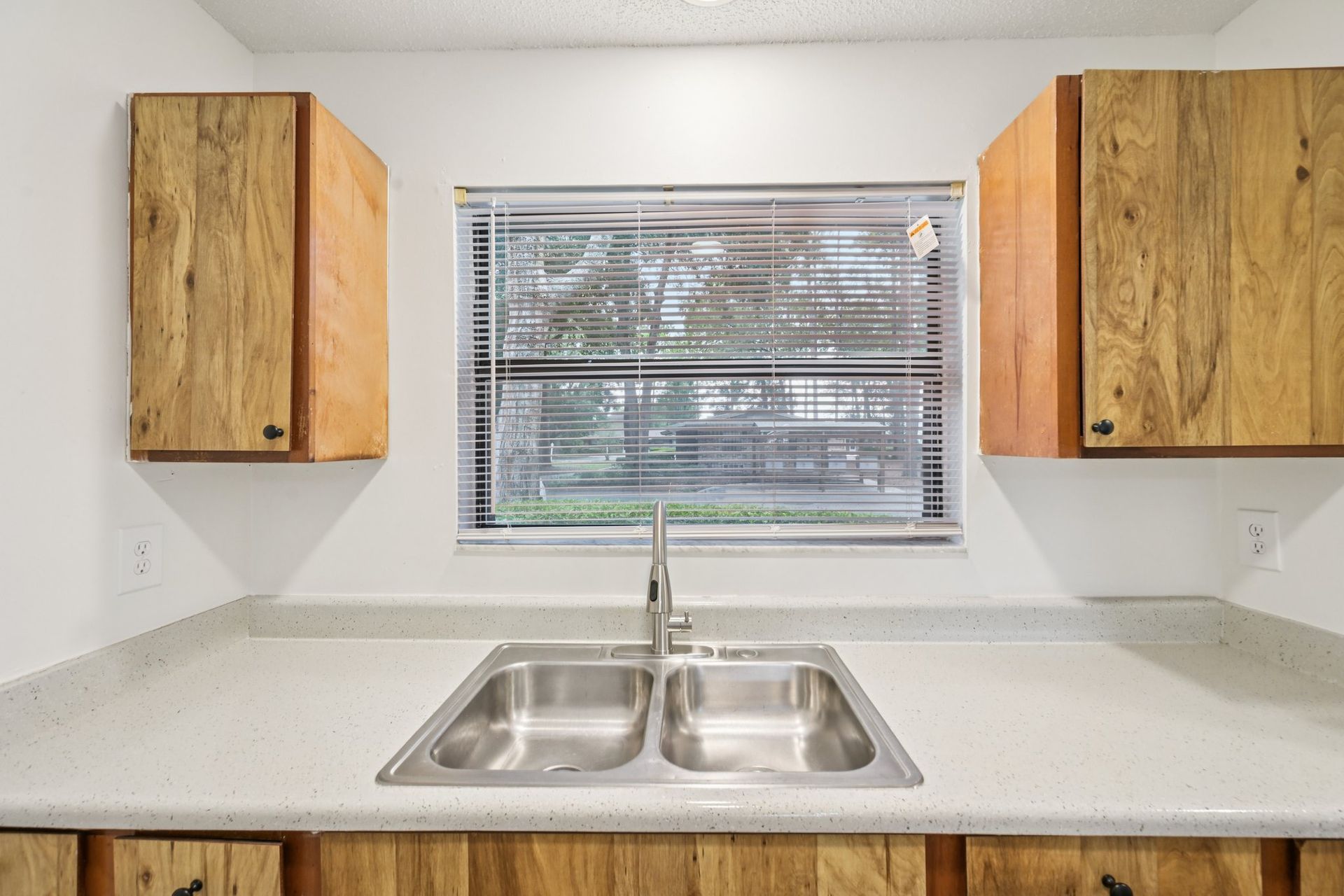 Kitchen sink with cabinets, window, and countertop. Natural wood cabinets, stainless steel sink.