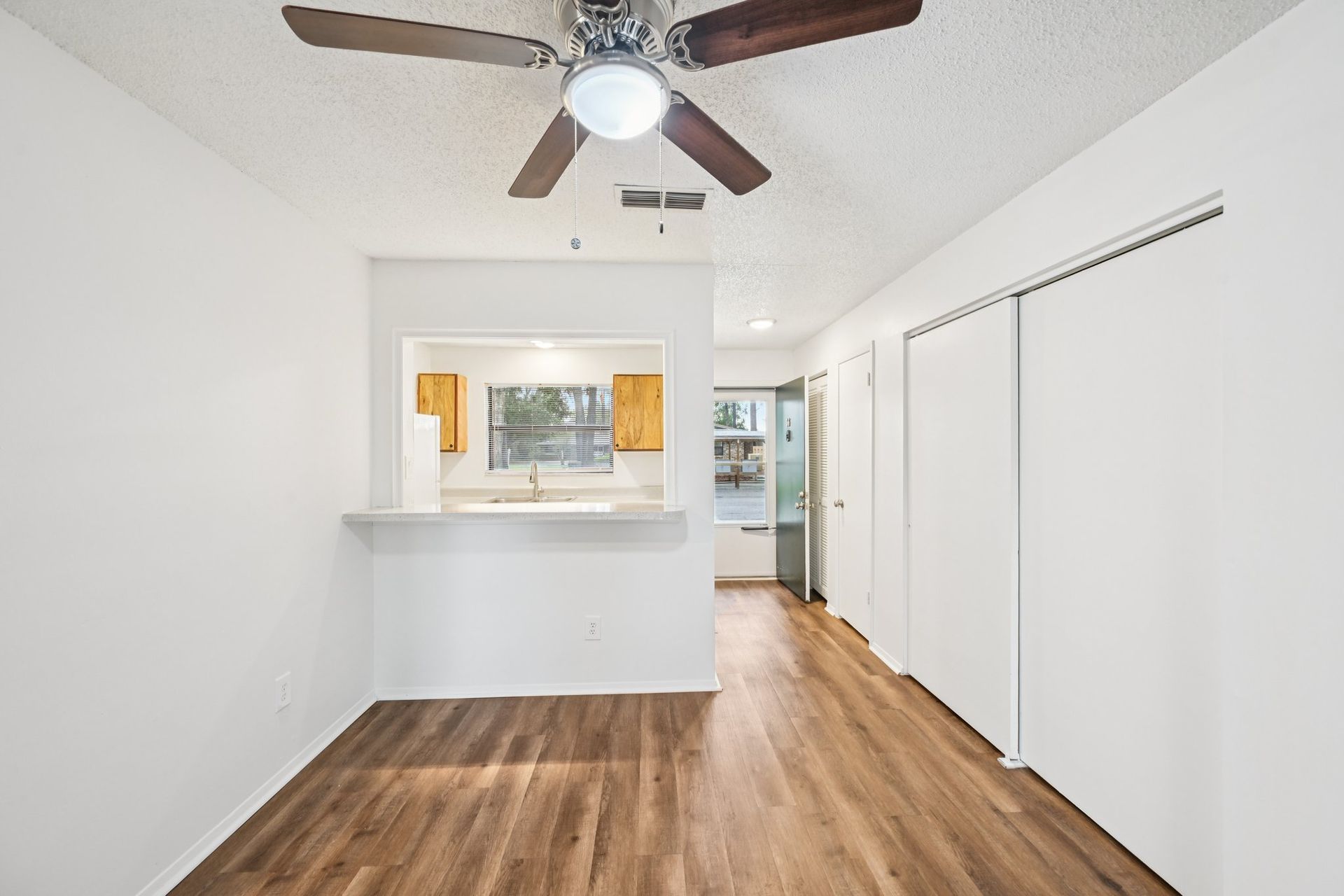 Empty dining area with white walls, wood floors, and pass-through to the kitchen.