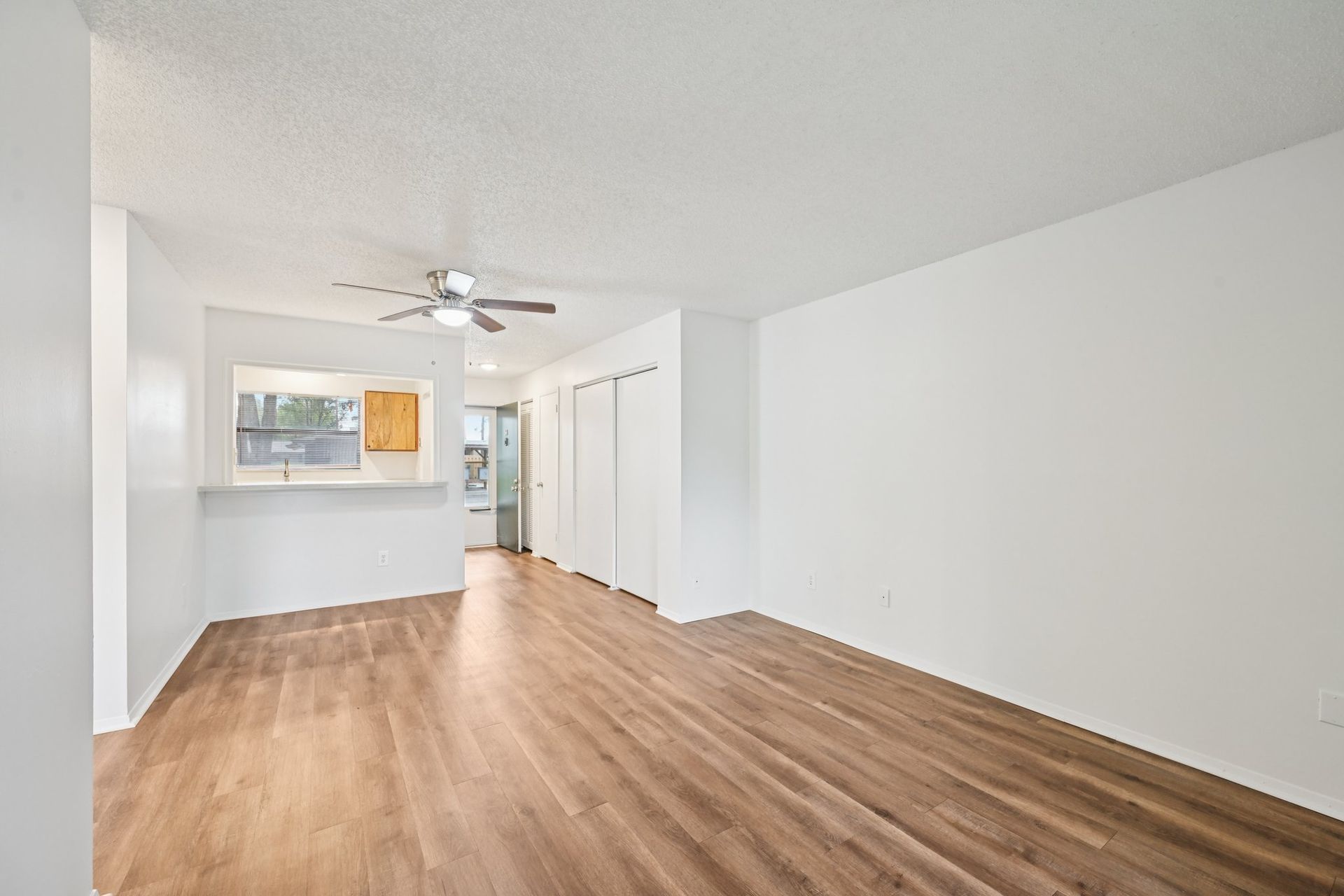 Empty living space with wood-look flooring, white walls, and a ceiling fan.