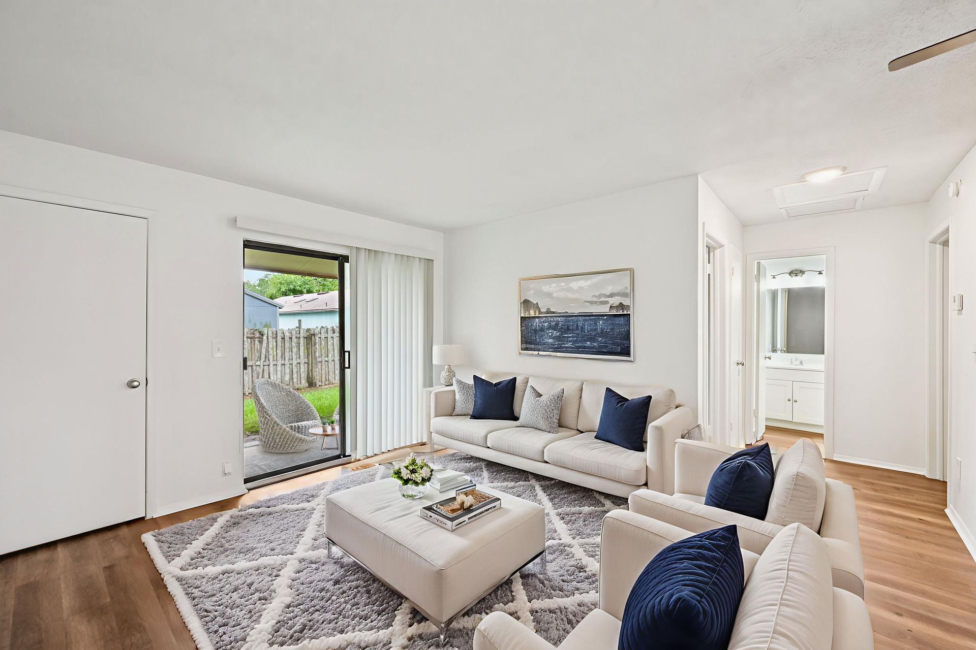 Living room with white walls, a beige sofa and chairs, an area rug, and a sliding door to the patio.