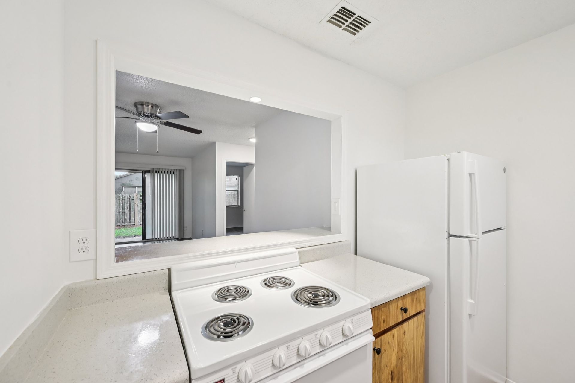 Kitchen with white appliances, countertop, and a pass-through window to the living area.