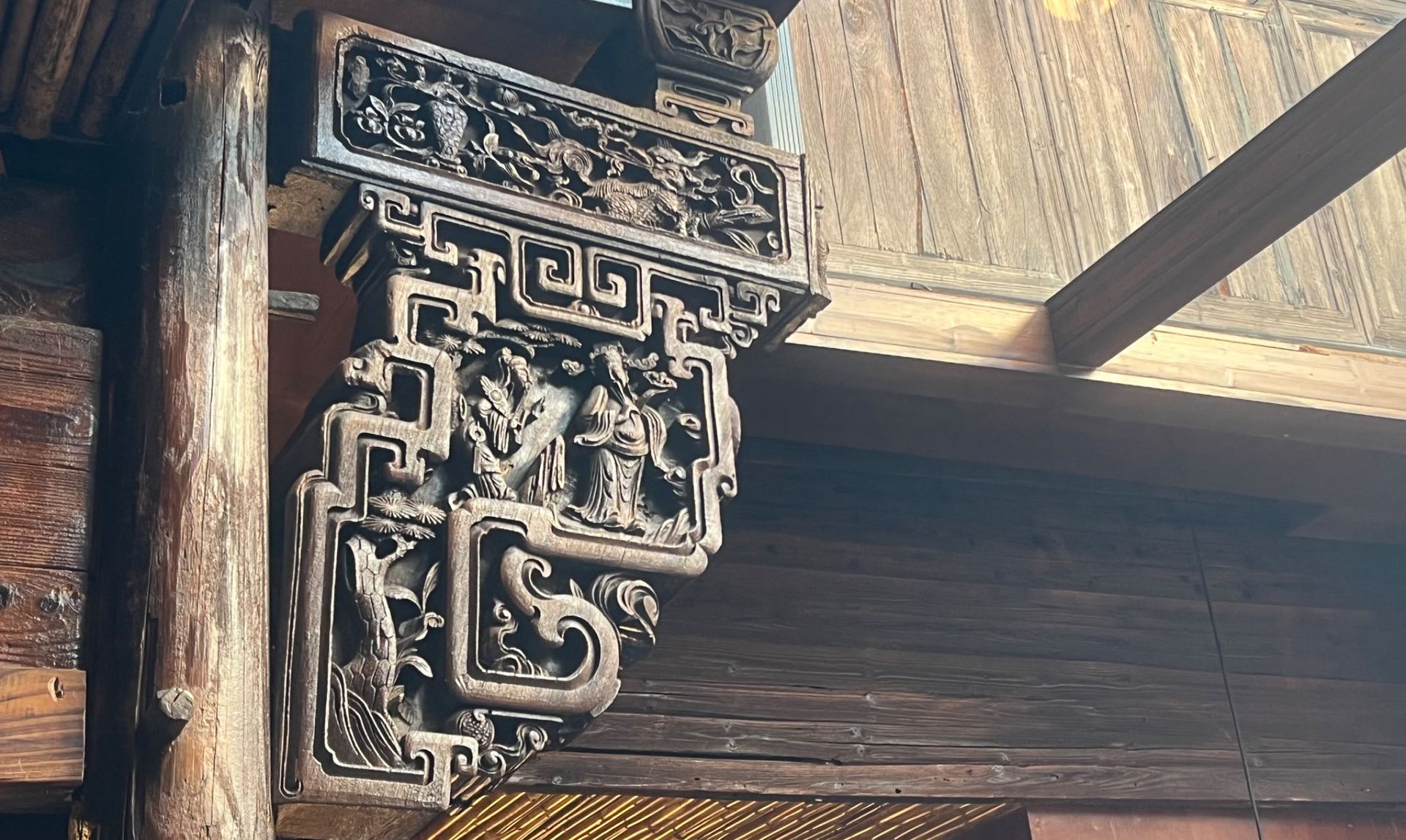 Ornate carved wooden bracket under a thatched roof beam in a rustic structure