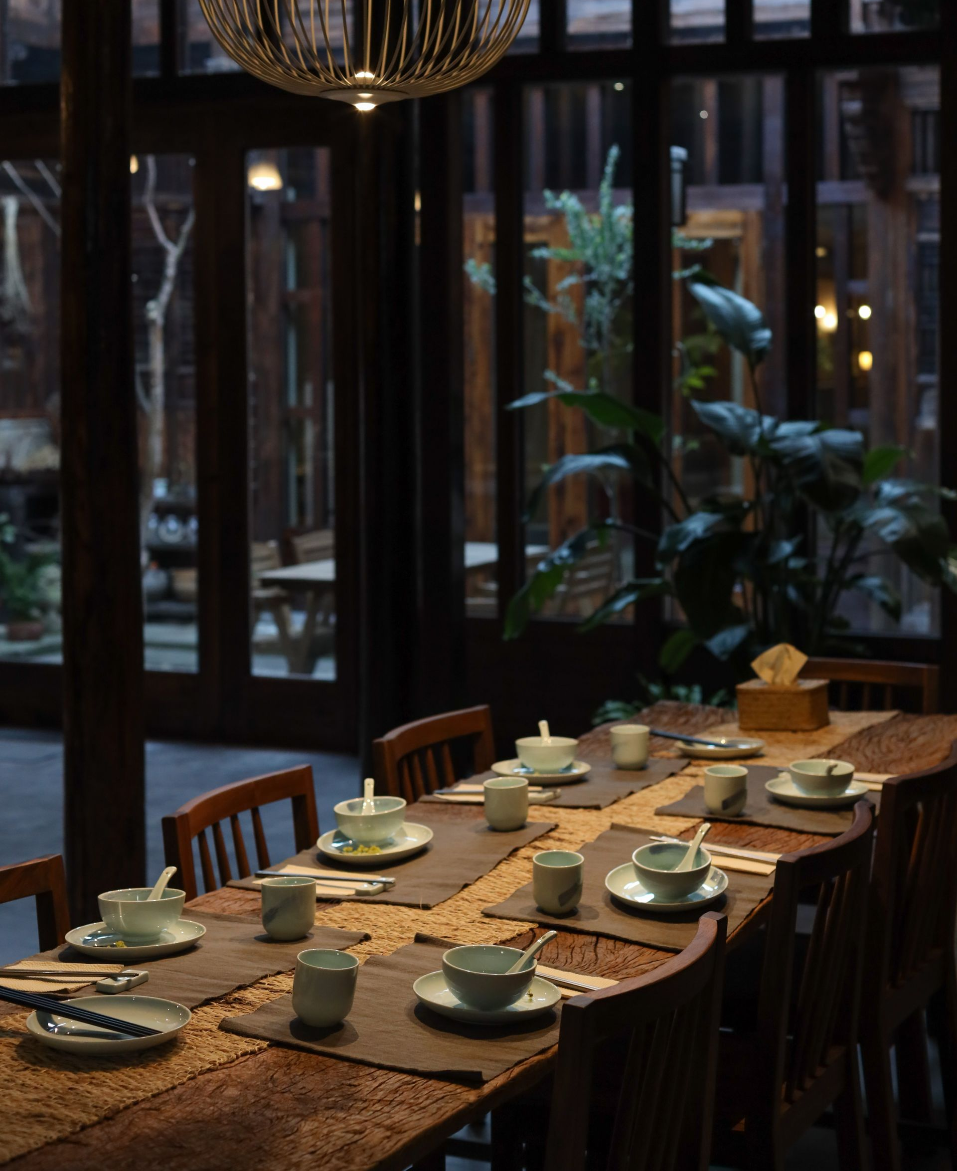Long dining table set with tea cups and plates in a dimly lit restaurant.