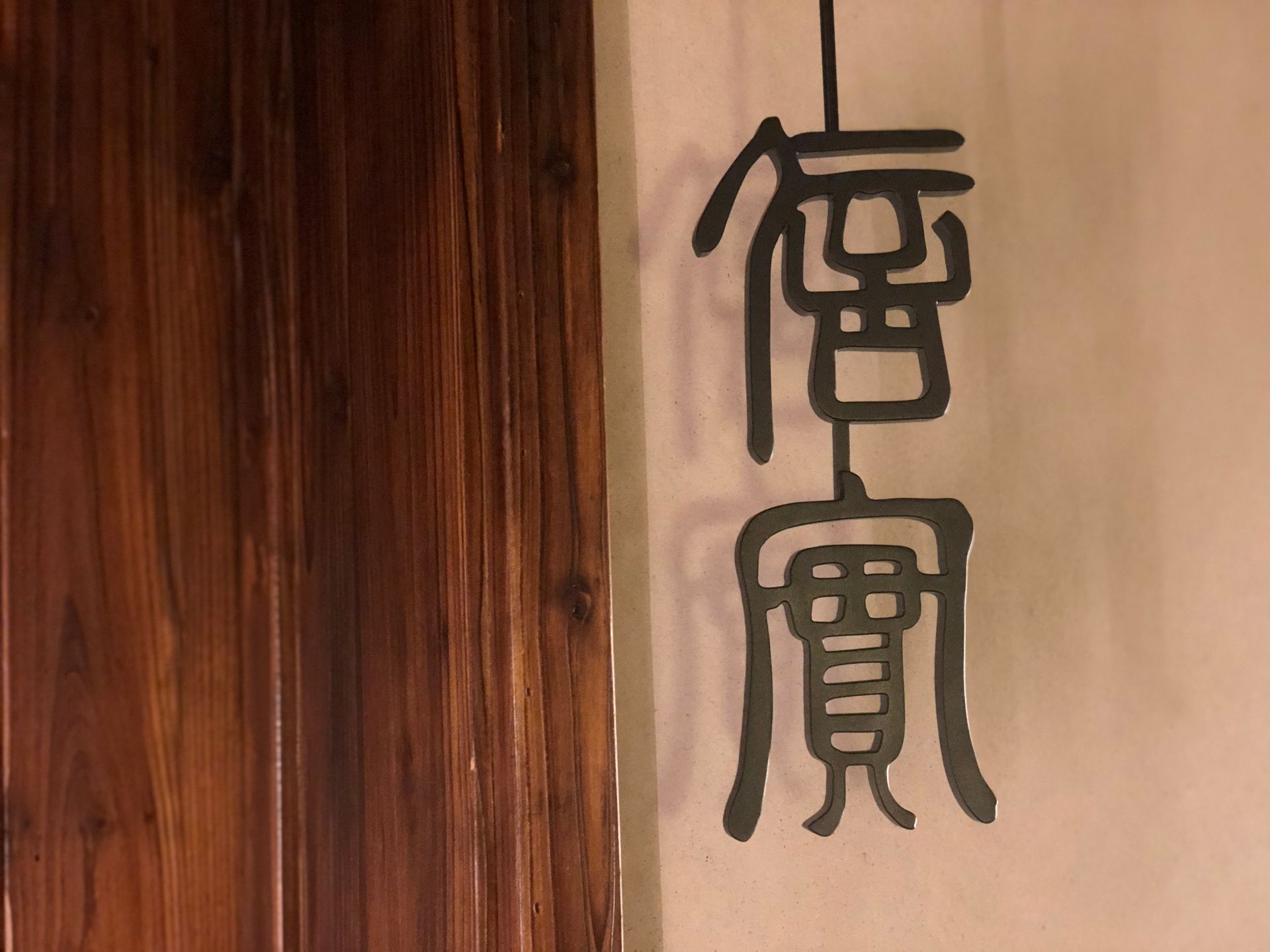 Vertical black calligraphy on beige wall beside a wooden panel.