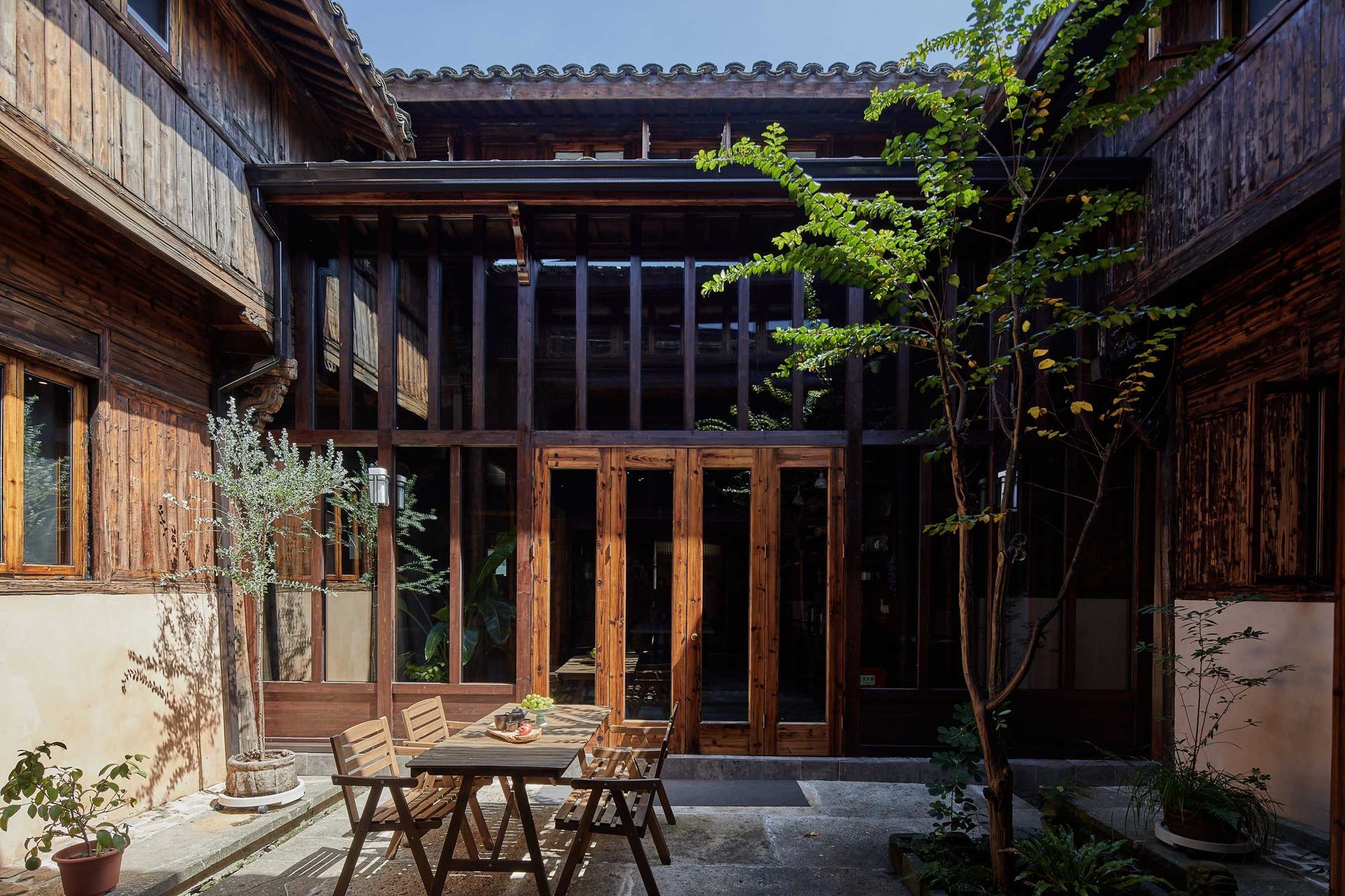 Courtyard with wooden doors, brick walls, and a small outdoor table under bright sunlight