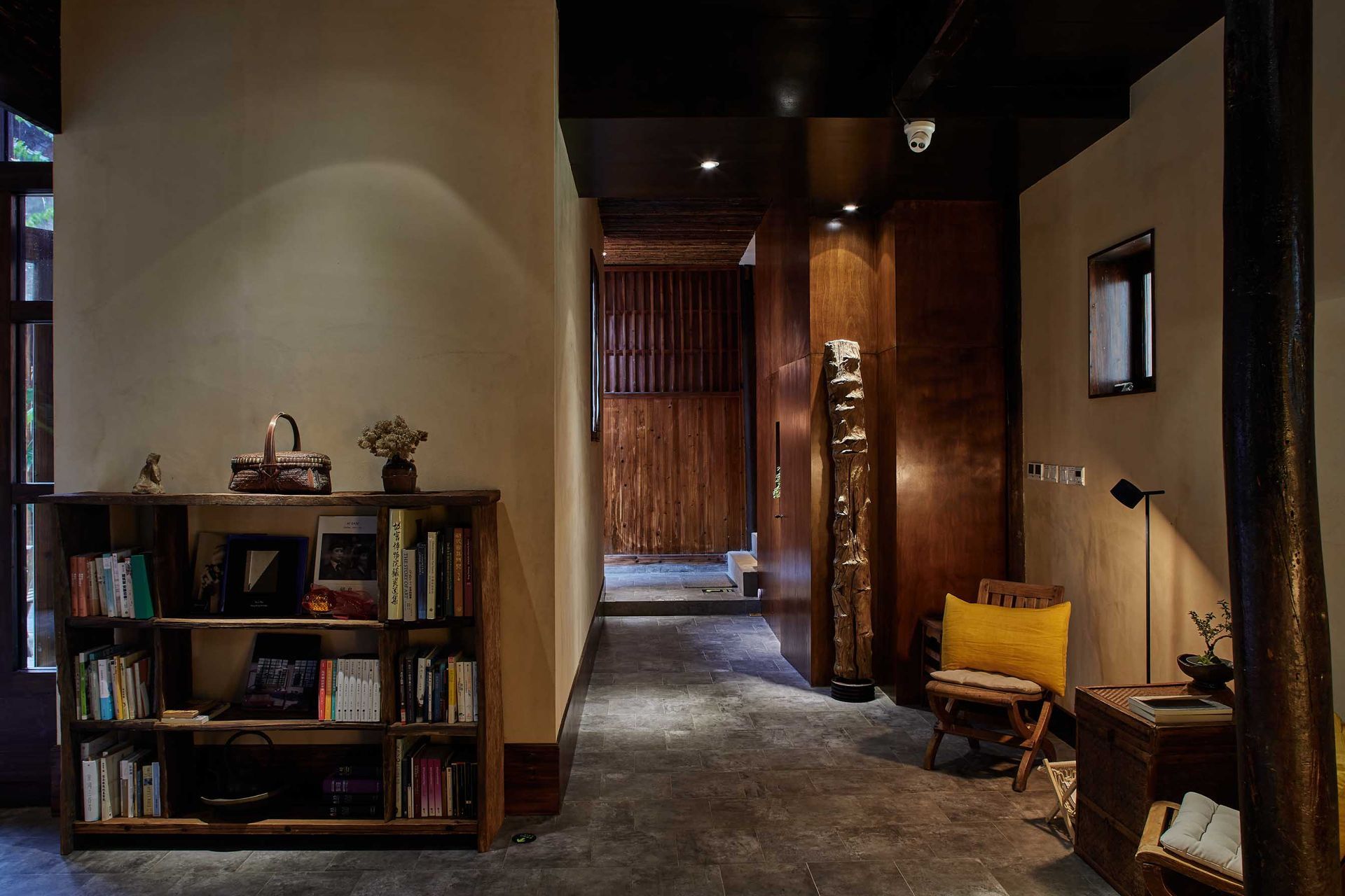 Dim hallway interior with bookshelves, warm lighting, and a yellow chair near a doorway