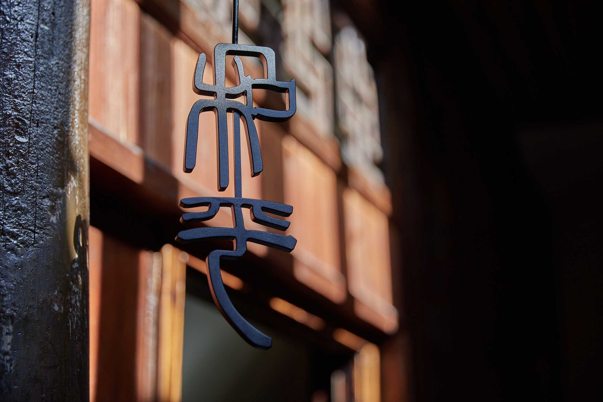 Blue hanging sign with Chinese characters beside a sunlit wooden window