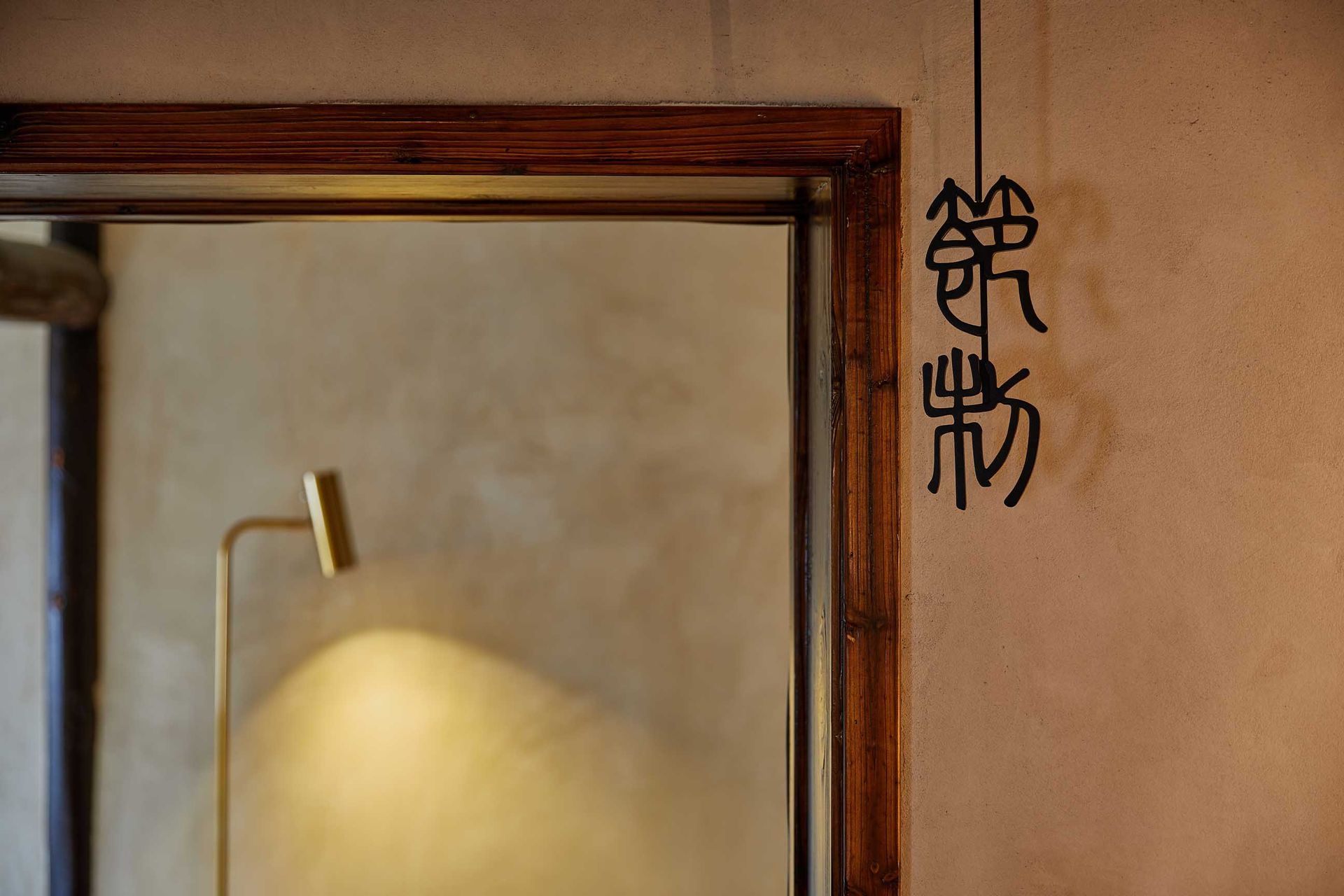 Wood-framed mirror beside a wall lamp, with black Japanese calligraphy on a peach wall