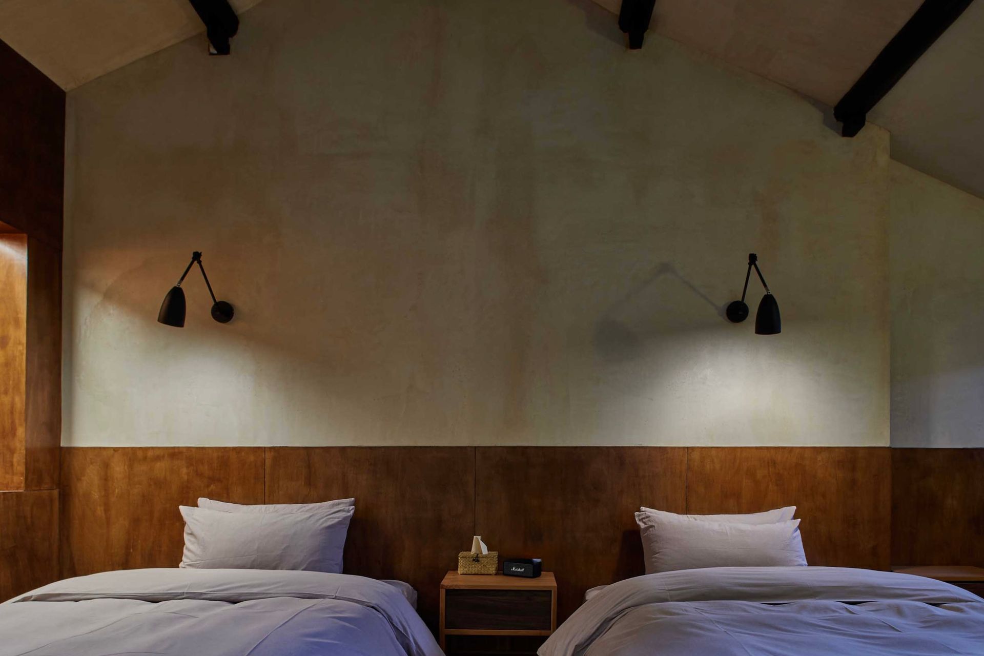 Twin beds in a rustic room with wood paneling, beige walls, and wall sconces