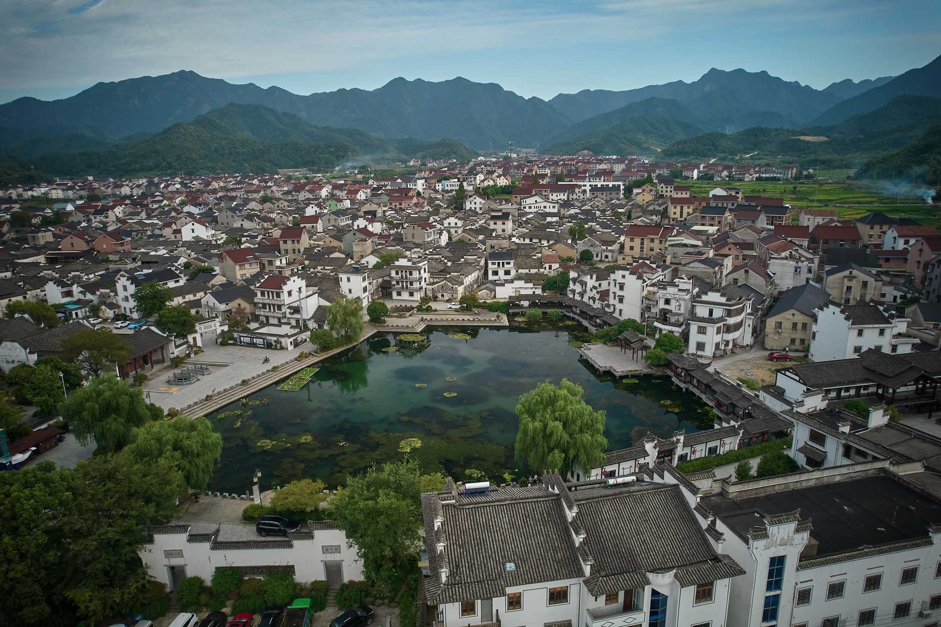 Aerial view of a town with a central pond, surrounded by houses and mountains in the distance