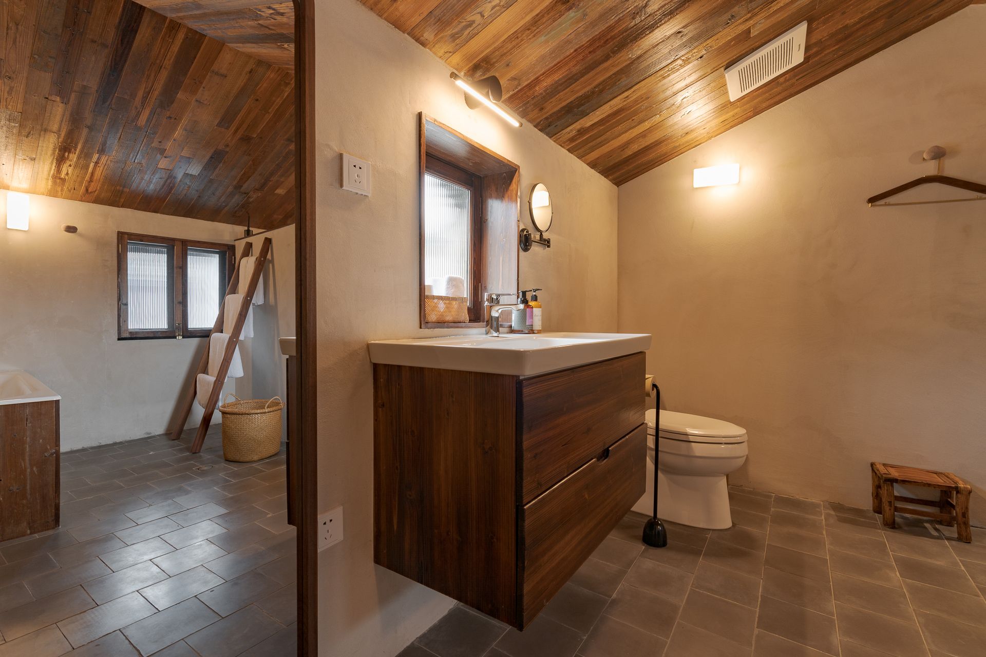 Small rustic bathroom with wood ceiling, tiled floor, vanity, toilet, and towel bar.