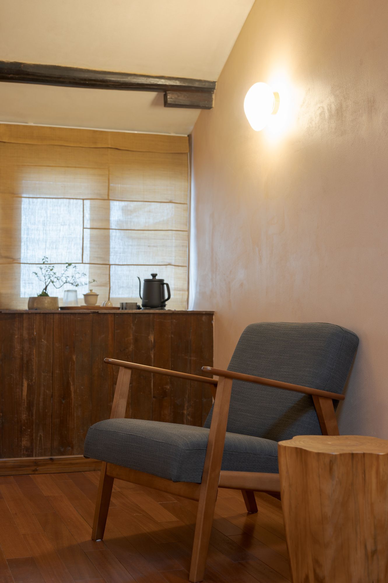 Cozy room with a blue armchair, wooden furniture, window with blinds, and a wall light.