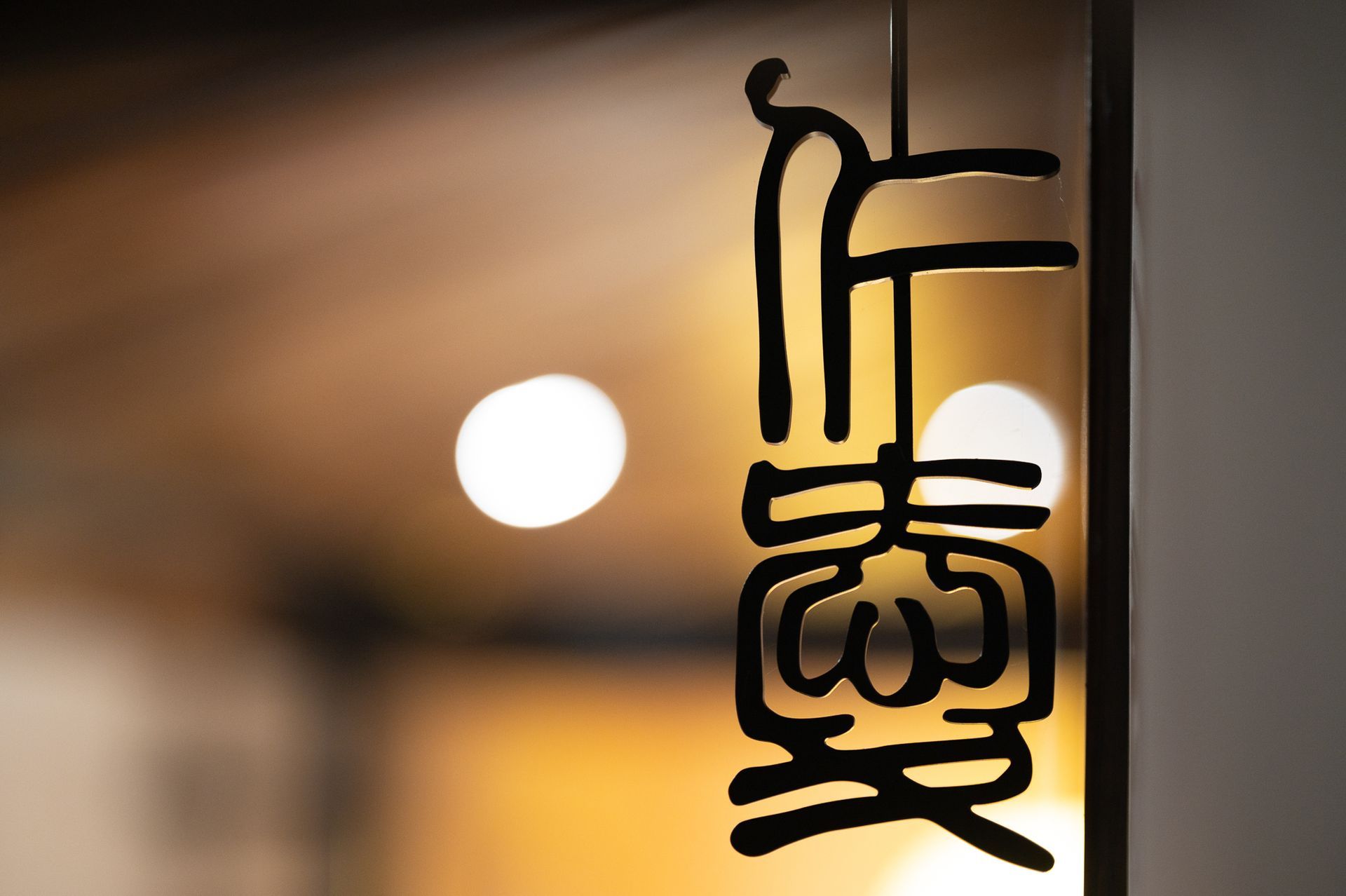 Glowing vertical neon sign with black lettering against a warm, blurred indoor background