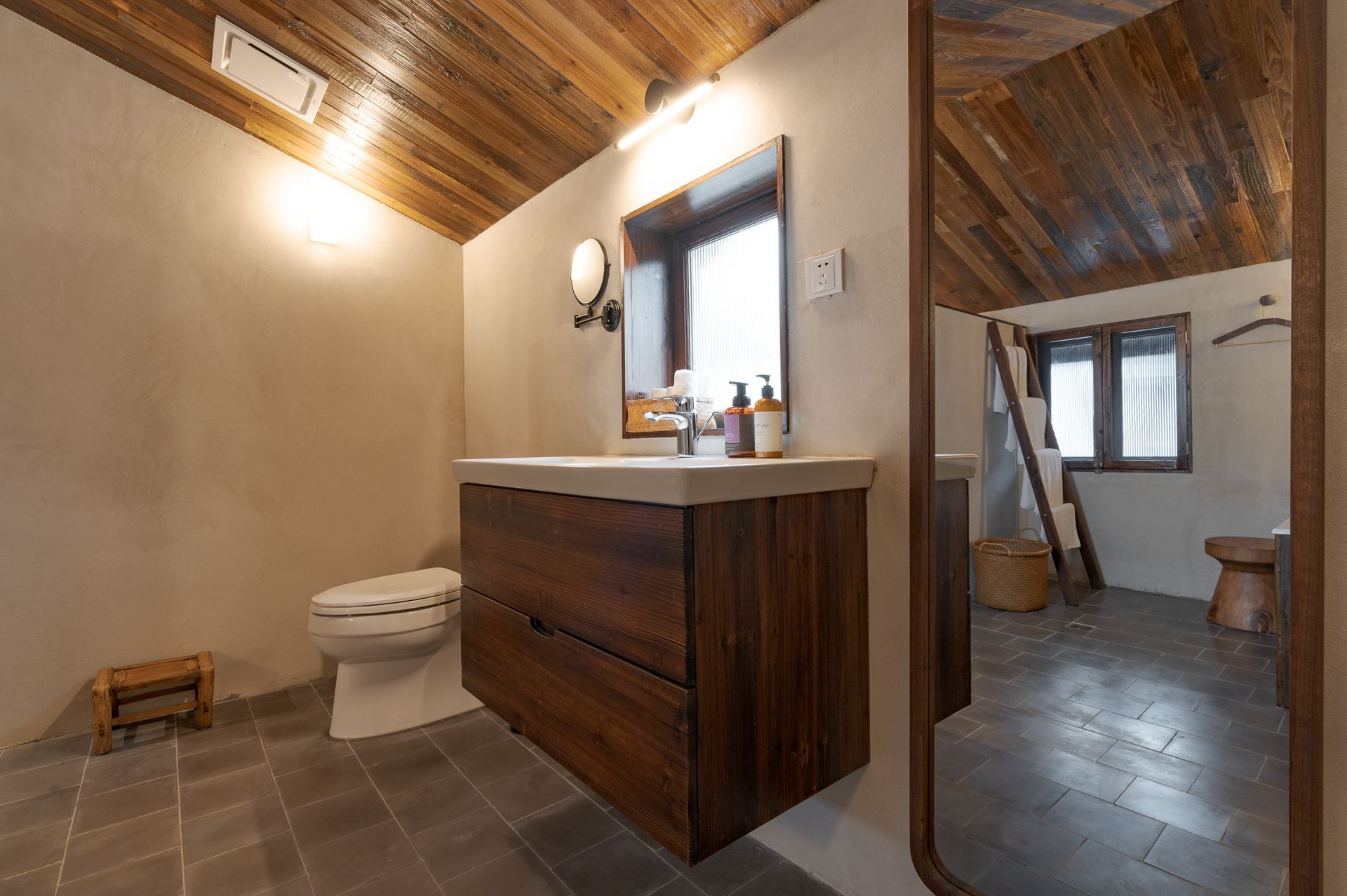 Bathroom with stone tile floor, wood ceiling, vanity sink, toilet, and open doorway to a bedroom.