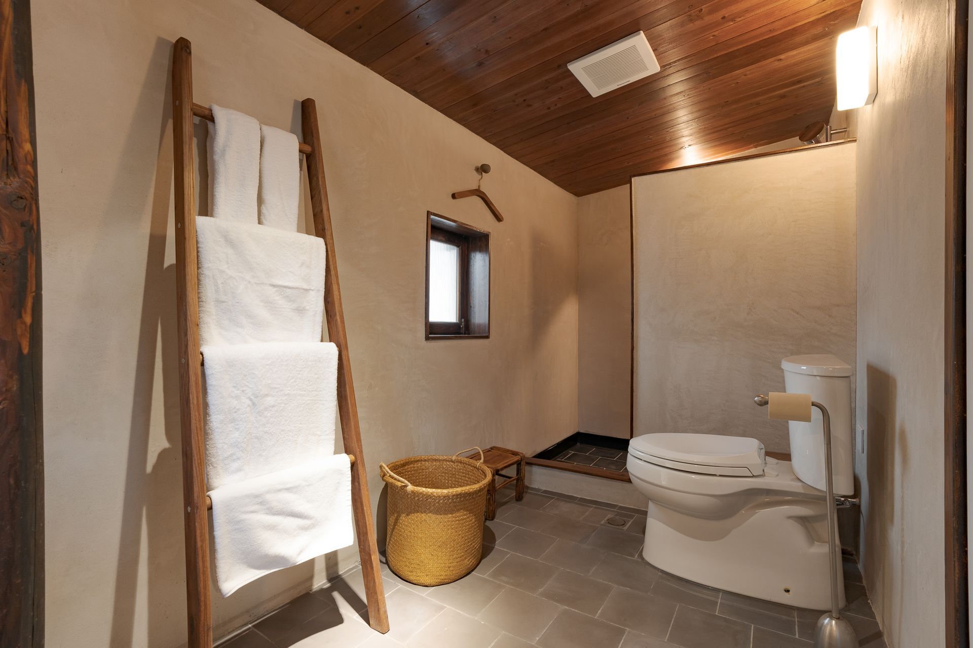 Small rustic bathroom with toilet, sink, shower, towels, and wicker basket.