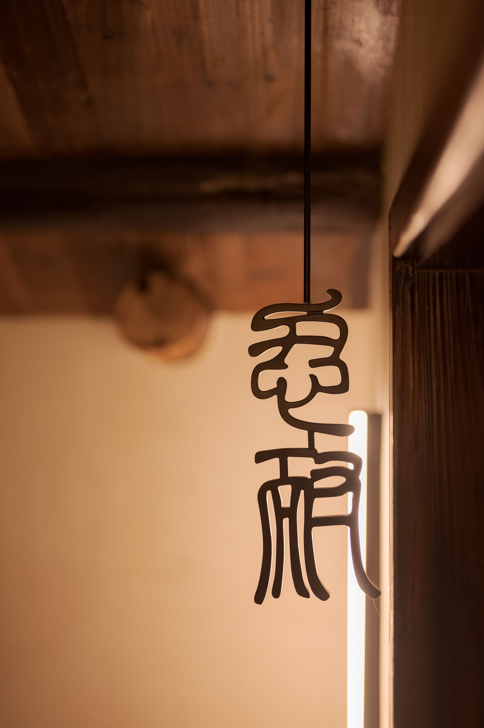 Hanging black Chinese calligraphy sign beside a warm-lit wooden ceiling.