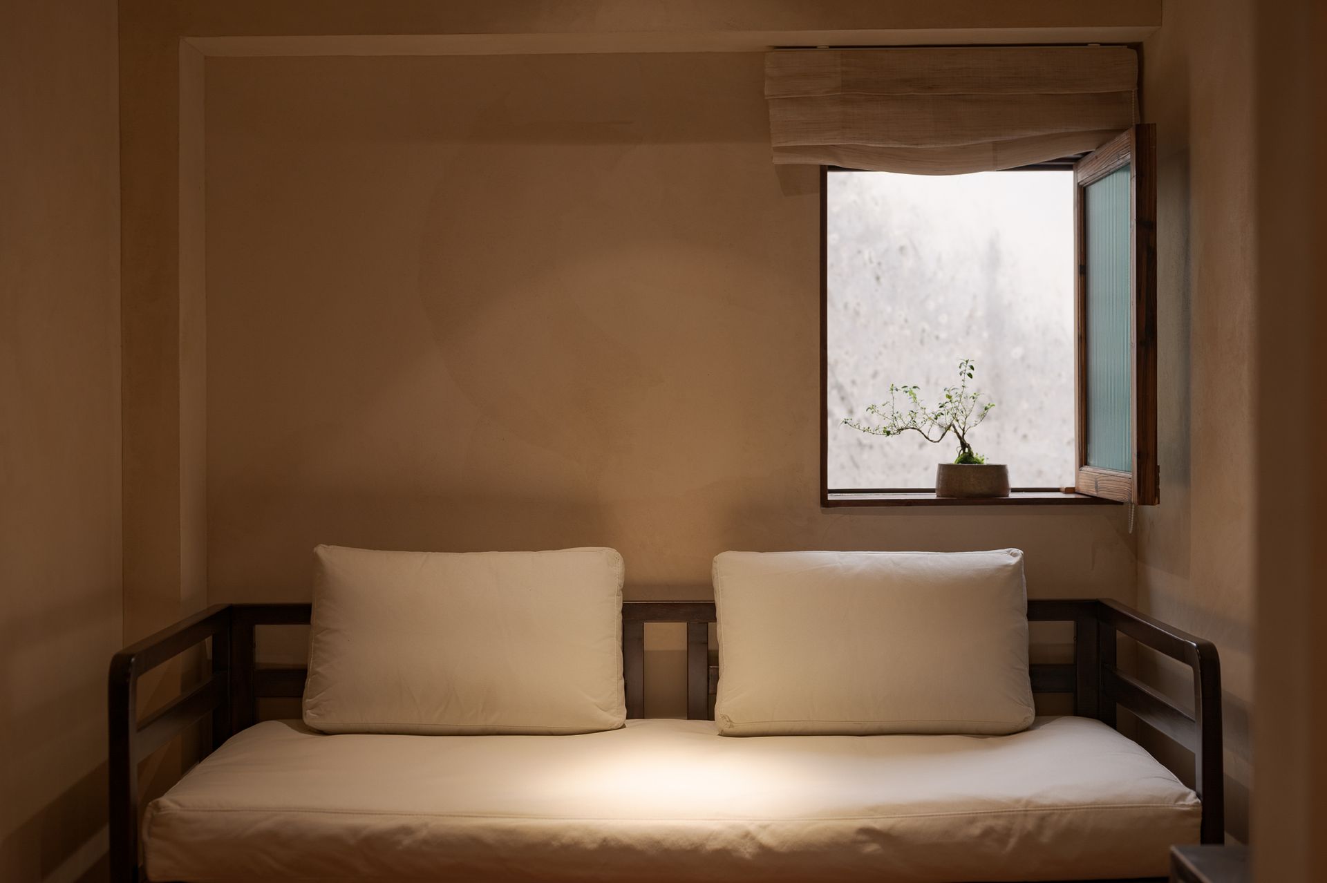Minimal bedroom with a white daybed, two pillows, and an open window with light curtains