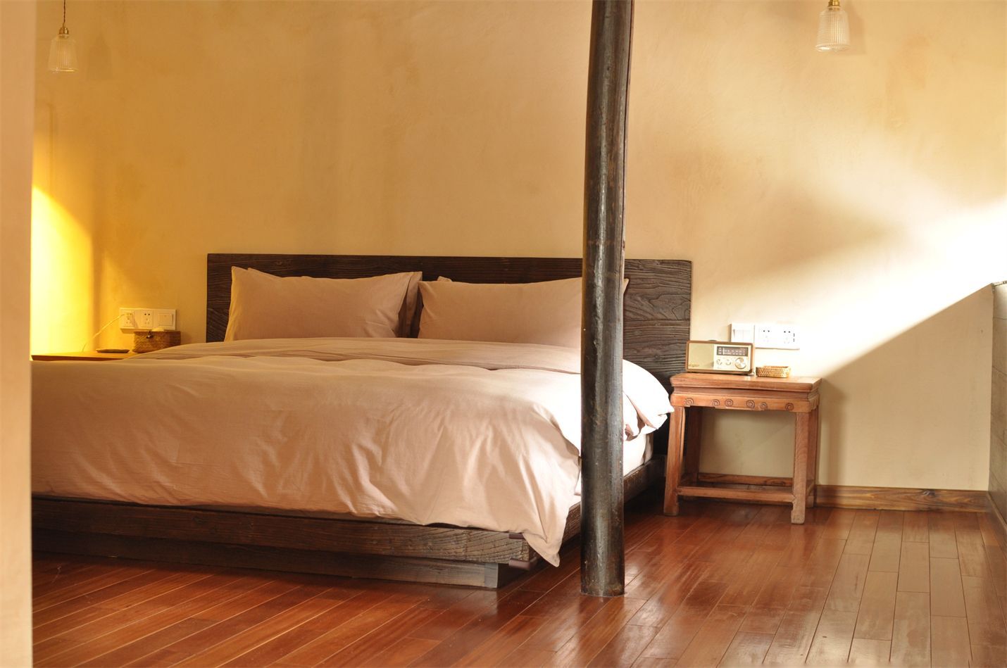 Cozy bedroom with a large bed, warm yellow walls, wooden floor, and a bedside table lamp