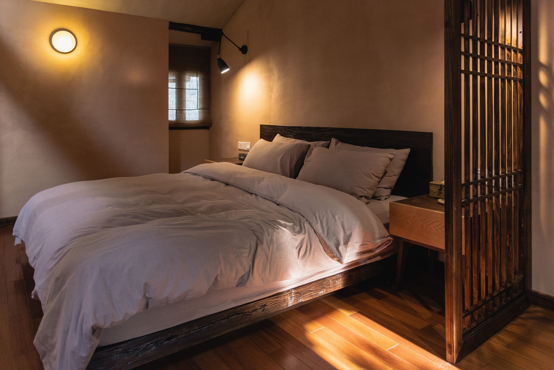 Cozy bedroom with a neatly made bed, warm lighting, and a wooden screen divider
