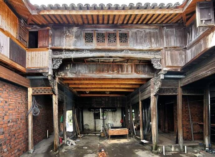 Old wooden courtyard with weathered beams, carved balconies, and a damp, empty ground floor