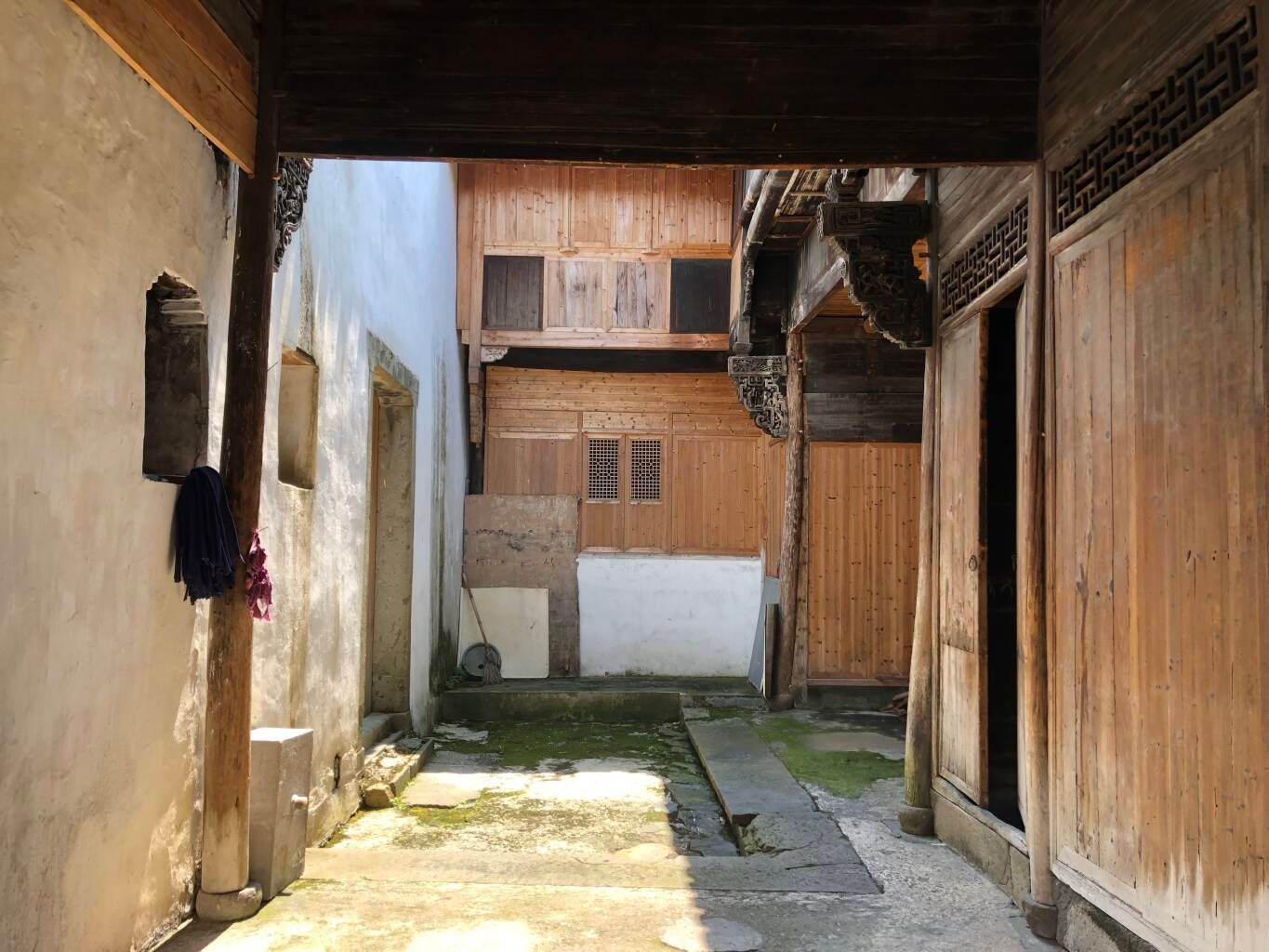 Narrow sunlit alley between wooden and concrete buildings with a few hanging items and weathered walls