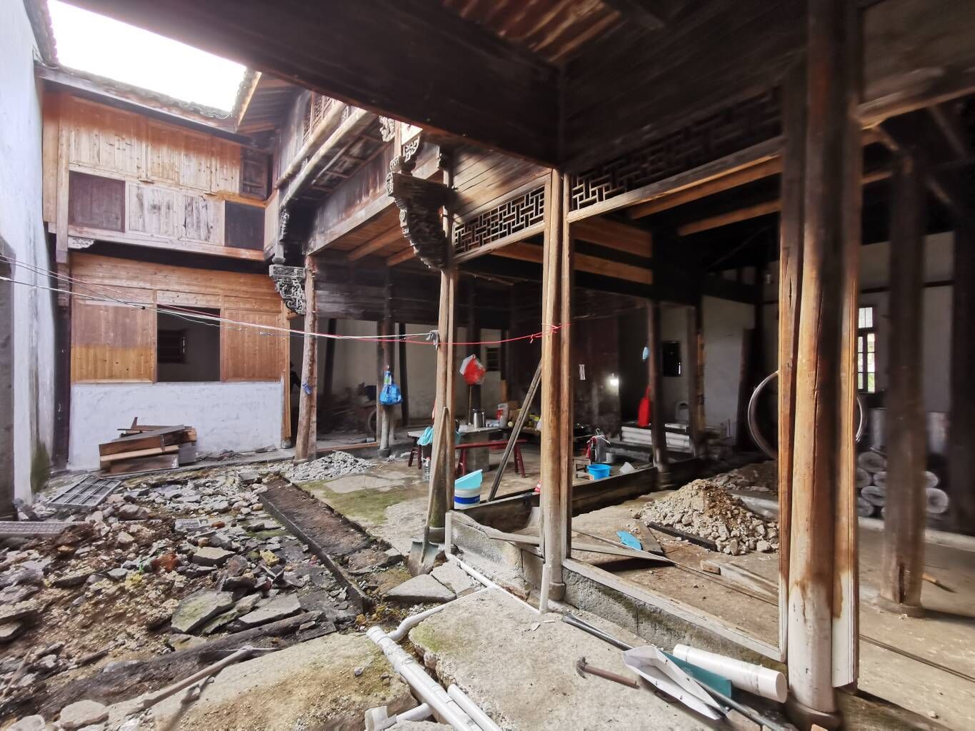 Dilapidated wooden courtyard with collapsed roof, debris, and exposed beams in an old building