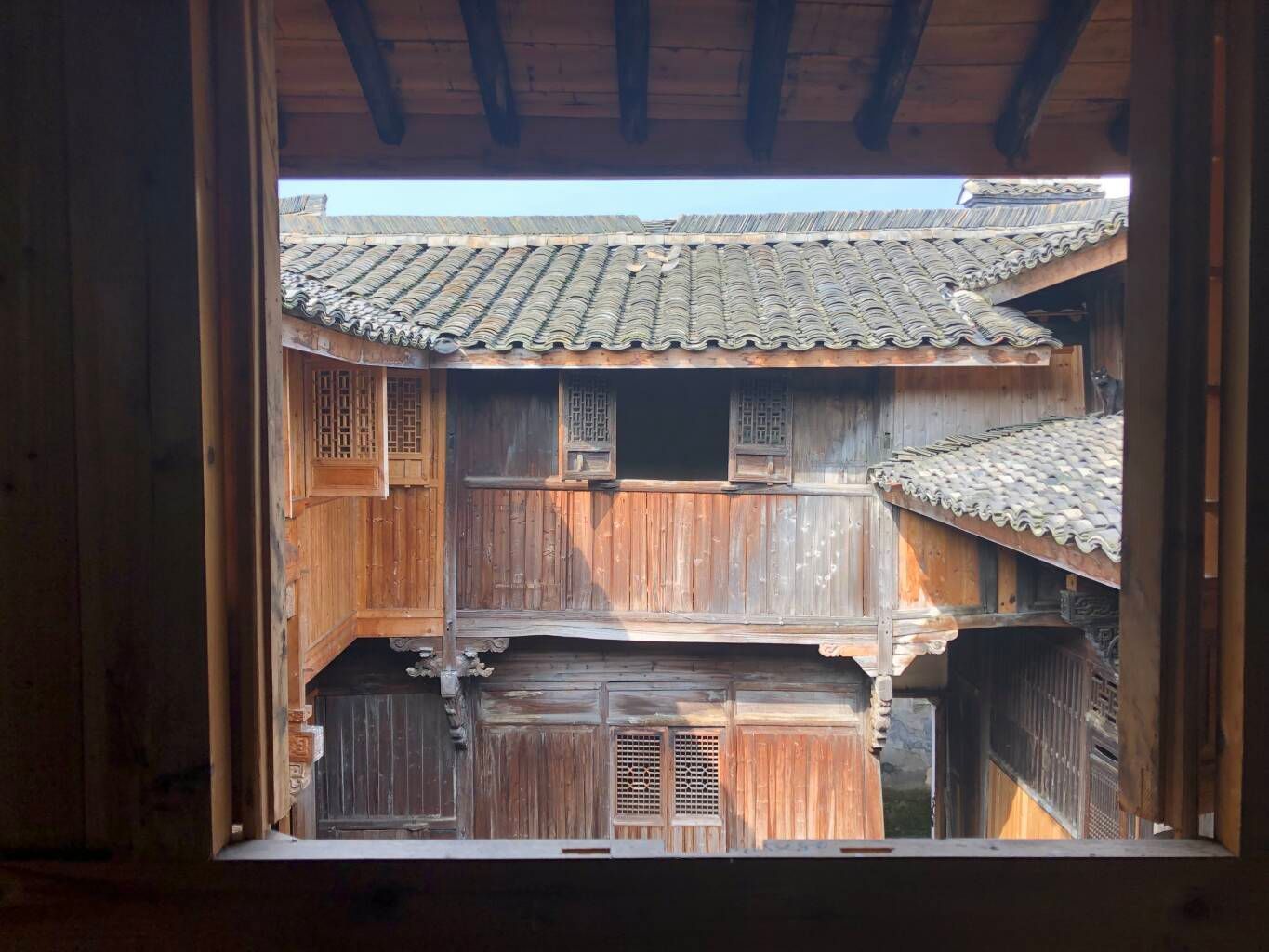 View from a window into a rustic wooden courtyard with tiled roofs and weathered buildings.