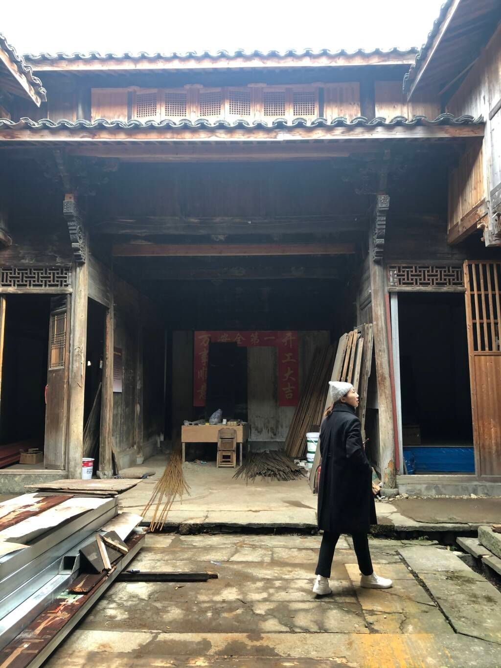 Person standing in a dim courtyard before a large wooden building with open doors and tiled roof