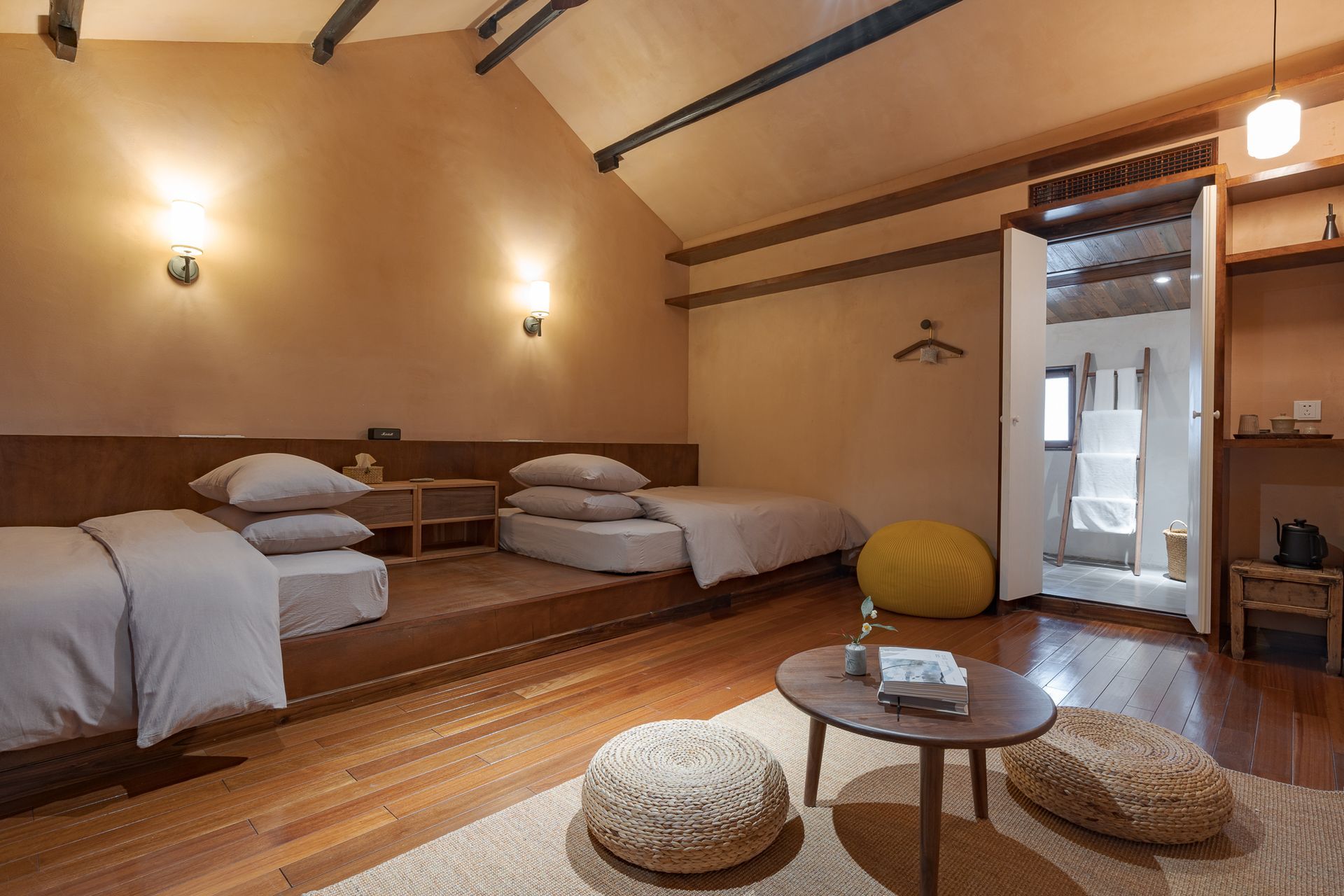 Cozy loft bedroom with two single beds, low wooden table, cushions, and warm lighting.