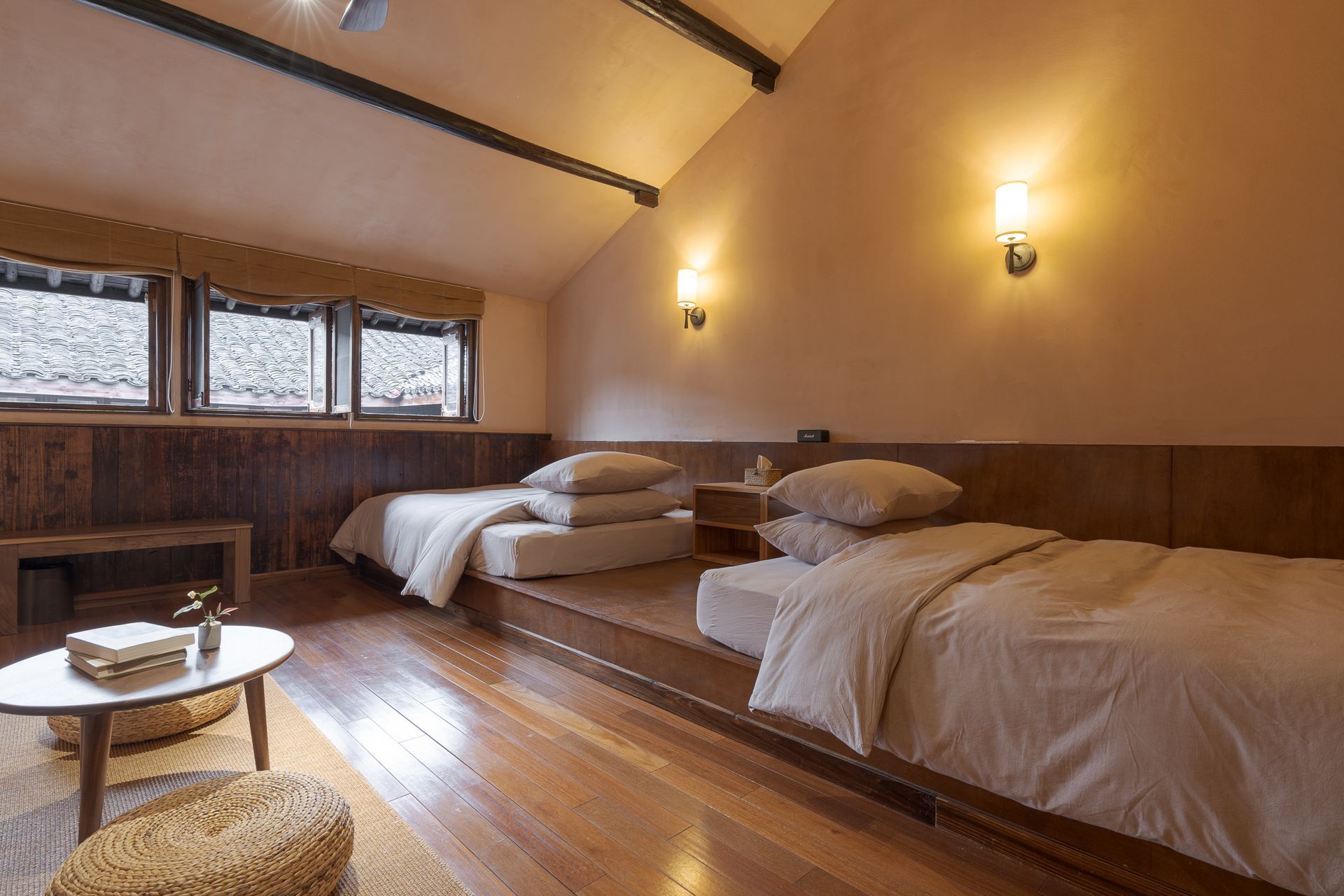 Cozy bedroom with three beds, wood floors, sloped ceiling, and warm wall lights by a window